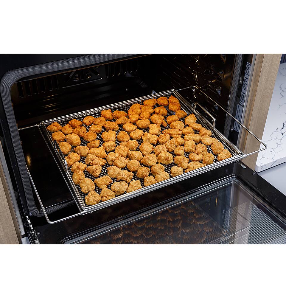 The image shows a toaster oven with a tray of food inside. The tray is filled with many small pieces of food, which appear to be breaded and fried. The oven is open, revealing the tray of food, and it seems to be in the process of cooking or reheating the food. The scene suggests that the oven is being used to prepare a meal or snack, possibly for a gathering or a quick meal for oneself.