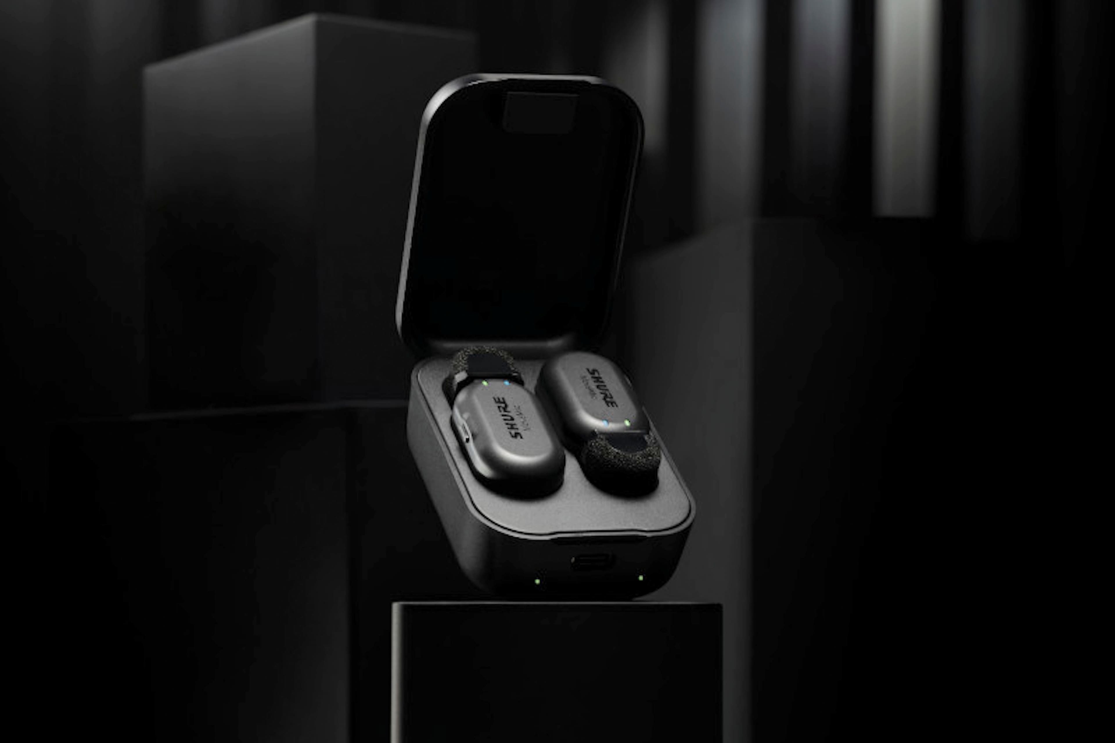 The image features a cell phone with a Mission Control app on the screen, which allows for direct-to-phone recording. The phone is placed on a table, and there are two earphones nearby. The ShurePlus MOTIV app enables users to access various features, such as speech mode, mute, and presets, to enhance their recording experience.