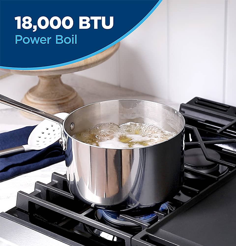 The image features a large silver pot sitting on top of a gas stove. The pot is filled with food, and it appears to be boiling. The stove is likely a gas range, as it is designed to provide high heat for cooking. The pot is placed on the stove's burner, which is likely to be a 18,000 BTU Power Boil, providing an efficient and powerful cooking experience. The stove is placed on a counter, and there is a bowl nearby, possibly for serving the cooked food.