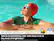 The image features a woman wearing a red swim cap and goggles, laying on her back in a pool of water. She appears to be enjoying her time in the water, possibly swimming or relaxing. The image is being used to advertise a product, likely related to swimming or water sports, as it is described as a "swimming advertisement." The advertisement claims to offer "100% Color Volume with Quantum Dot," which suggests that the product may be a high-quality, colorful swimwear or swimming accessory.