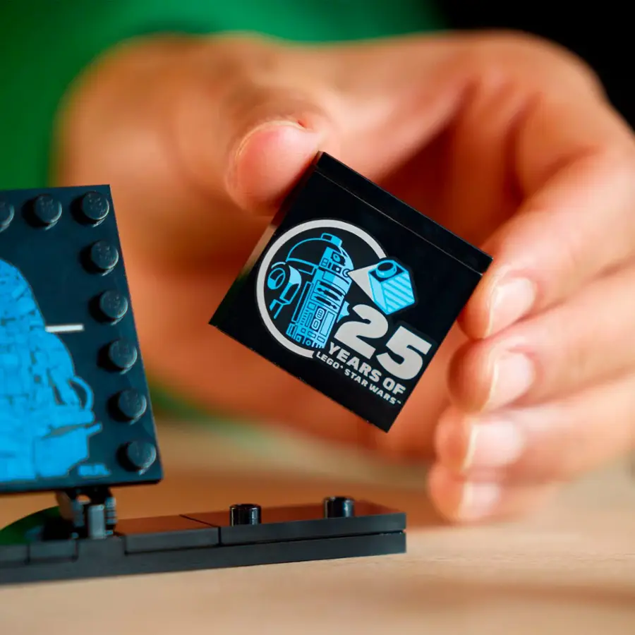 The image shows a person holding a small Lego piece, which is a celebration of 25 years of Star Wars. The person is holding the Lego piece in their hand, showcasing the tiny size of the commemorative piece.