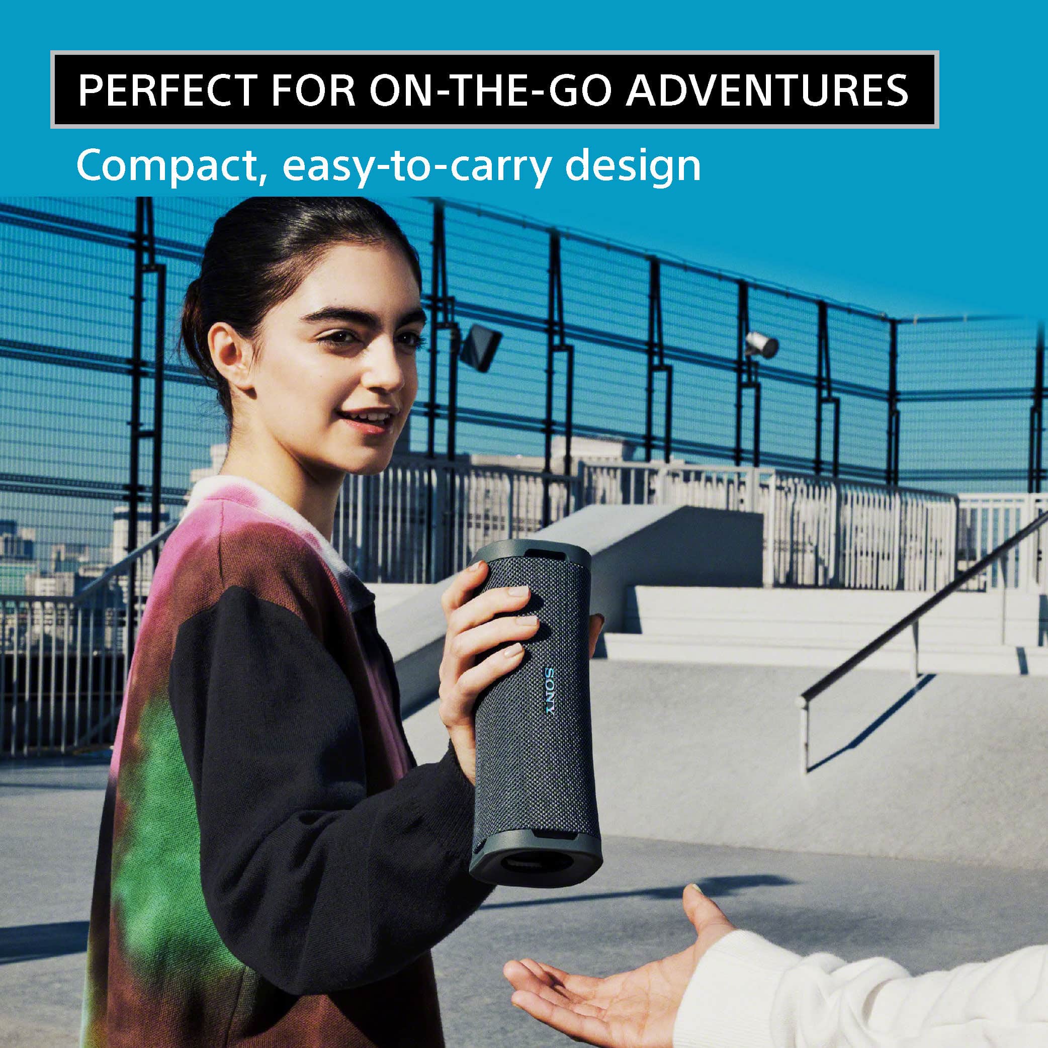The image features a woman holding a compact, easy-to-carry device, likely a portable speaker or a water bottle, while standing next to a man. The woman is wearing a black and white sweater, and the man is extending his hand towards her. The scene suggests that the device is perfect for on-the-go adventures, as it is compact and easy to carry.