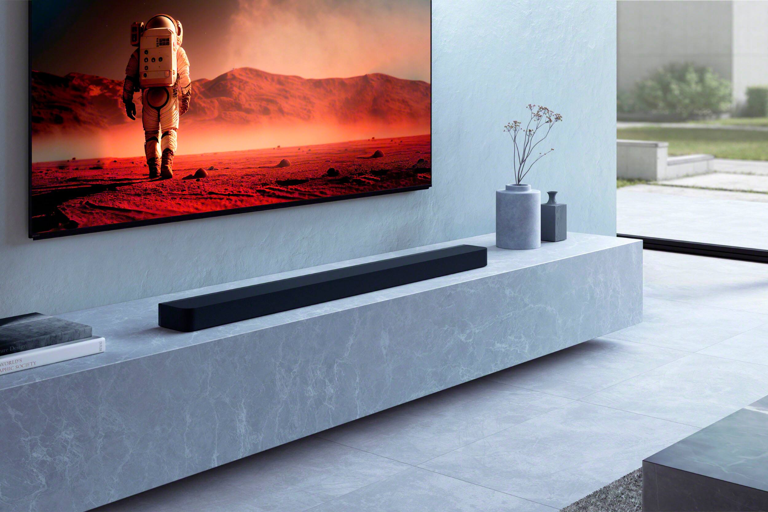 The image features a large flat screen TV mounted on a wall in a modern living room. The TV is displaying a picture of a man in a space suit, possibly from a movie or a TV show. The room has a sleek and minimalist design, with a long bench and a vase placed nearby. The overall atmosphere of the room is clean and well-organized, with the TV being the focal point of the space.