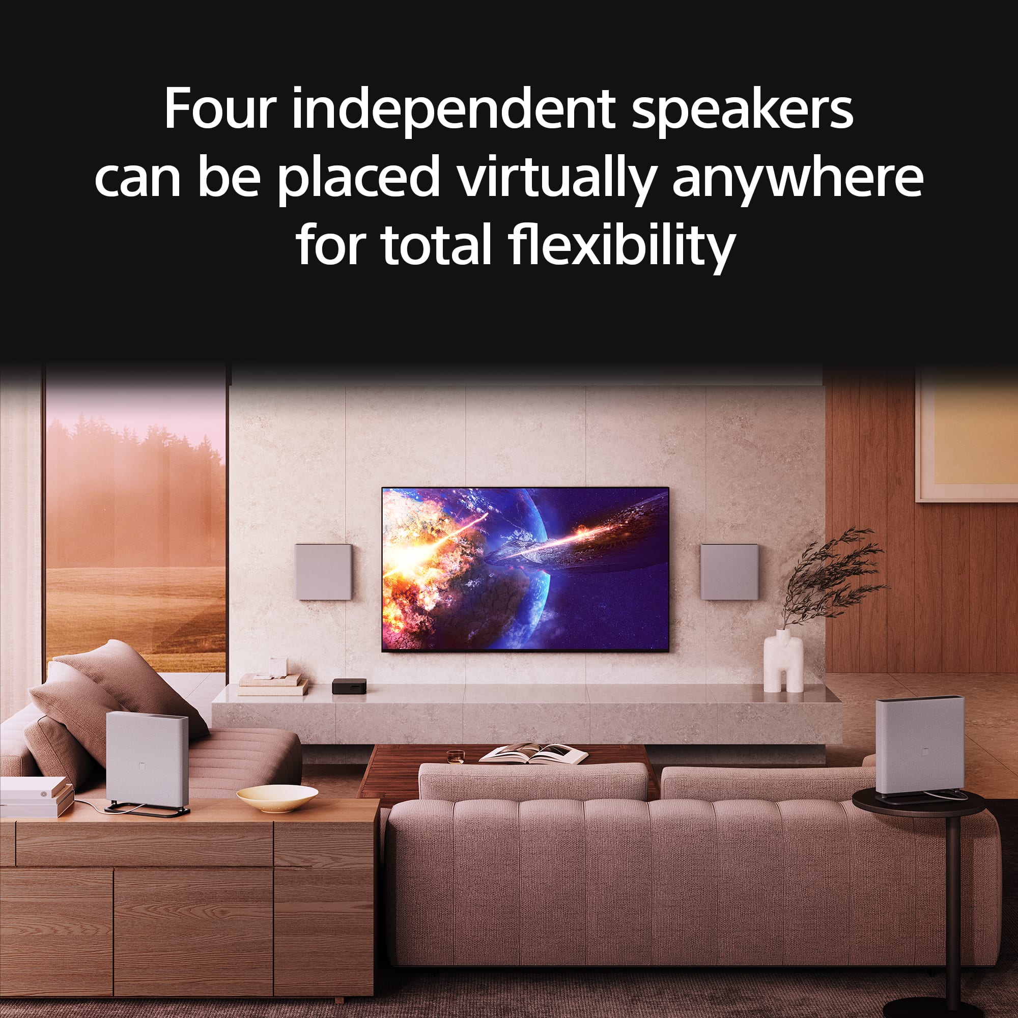 The image features a living room with a large flat screen TV mounted on the wall. There are four independent speakers placed around the room, which can be positioned virtually anywhere for optimal flexibility. The living room is furnished with a couch and a potted plant, creating a comfortable and inviting atmosphere.