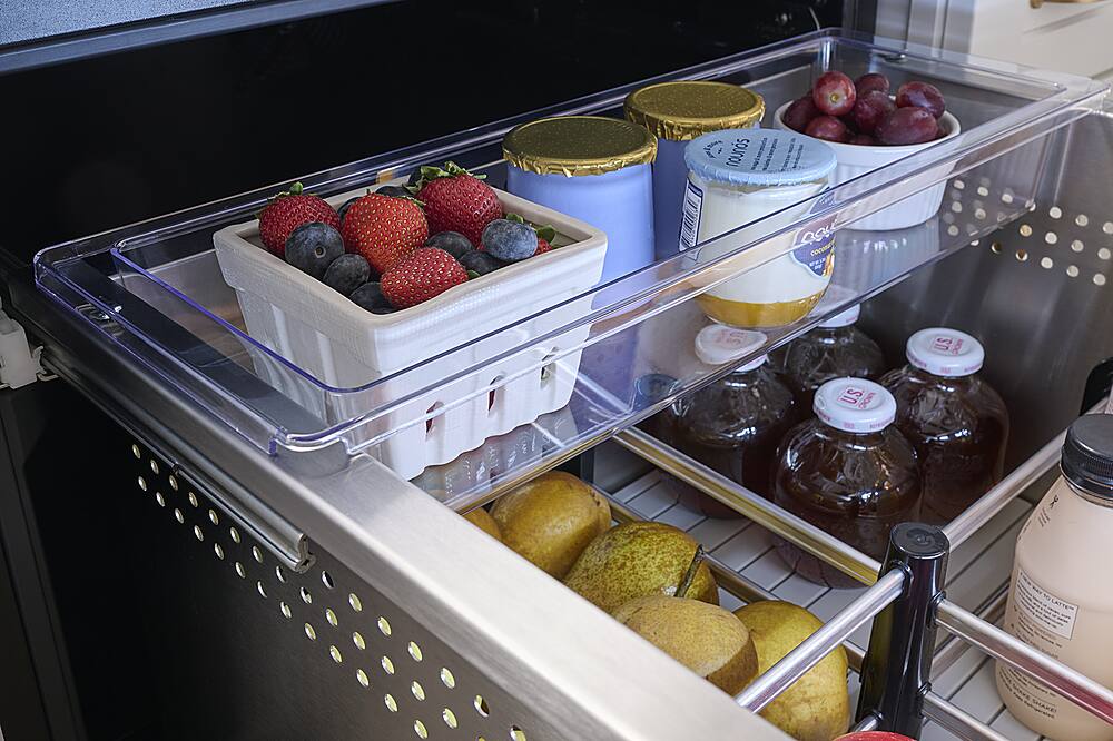 The image shows a refrigerator with a variety of food items stored in it. There are several containers of yogurt, as well as a basket of fruit that includes strawberries, blueberries, and grapes. Additionally, there are jars of jam and a container of butter. The refrigerator is well-stocked and organized, making it a convenient place to store and access food items.