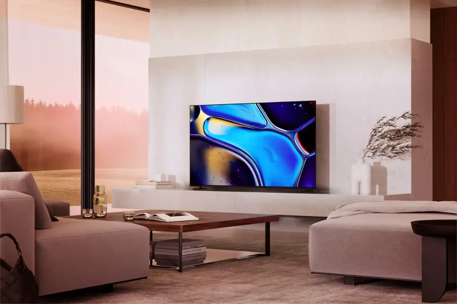 The image features a large flat screen TV mounted on a wall in a living room. The TV is positioned between two couches, with one couch on the left side and the other on the right side of the room. The room also includes a dining table, a few chairs, and a potted plant. There are several bottles placed around the room, and a handbag can be seen on the floor. The overall scene is a well-furnished living space with a focus on entertainment and relaxation.
