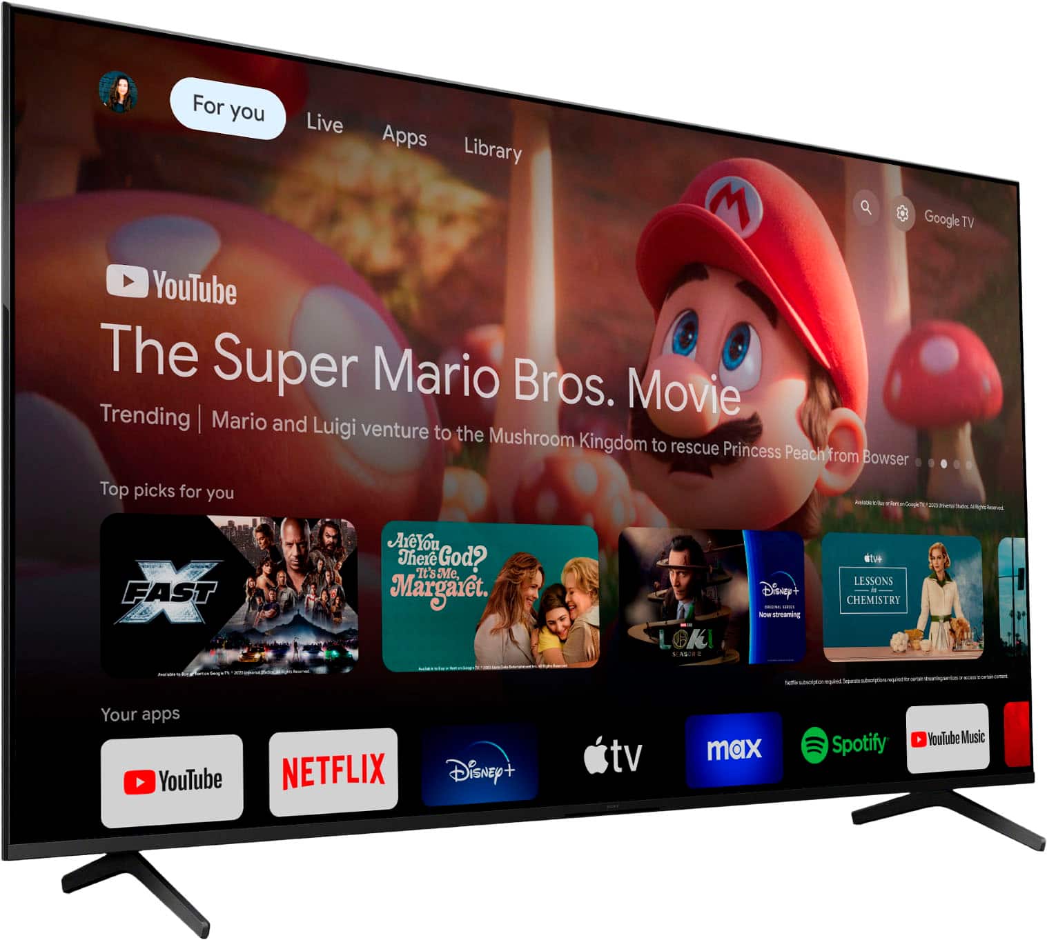 The image features a large flat screen TV displaying various apps, including YouTube, Netflix, Disney+, and Spotify. The TV is promoting the Super Mario Bros. movie, and there are icons for different channels and movies on the screen. The TV is placed on a stand, and the display is quite prominent, showcasing the various options available for entertainment.