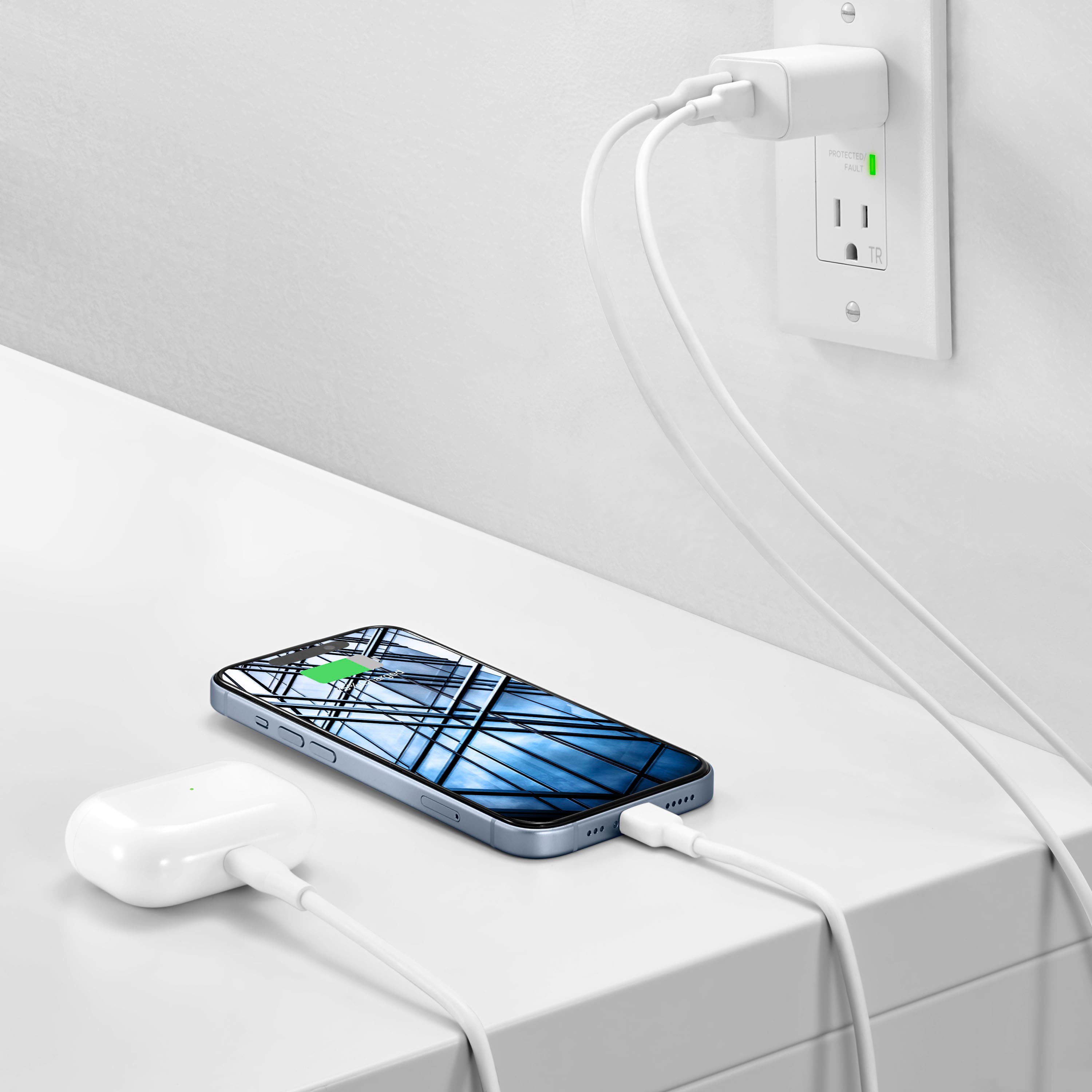 The image shows a cell phone sitting on a table, connected to a charger. The charger is plugged into an outlet, providing power to the phone. The phone is positioned near the edge of the table, and the charger is located on the left side of the phone. The outlet is located on the right side of the phone, and the cords are visible, connecting the charger to the phone and the outlet.
