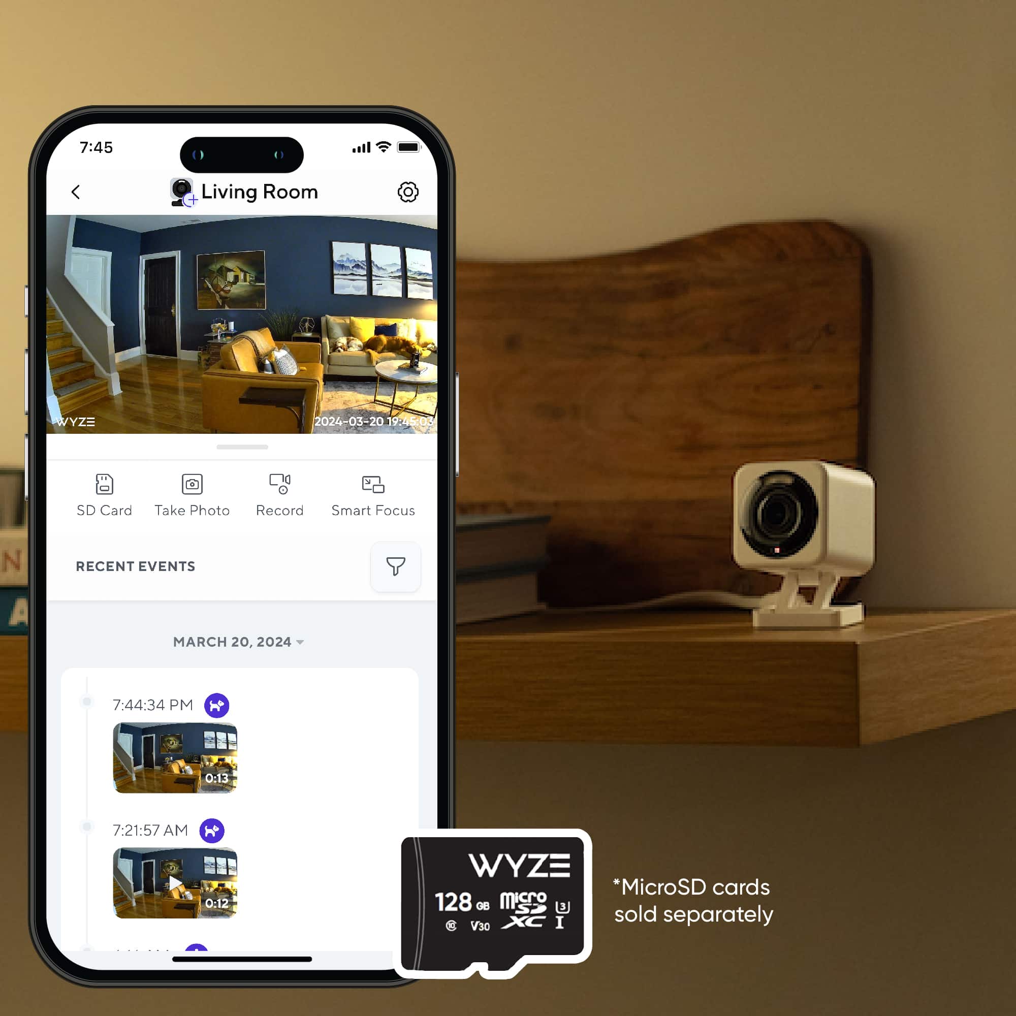 The image features a cell phone displaying a photo of a living room. The phone is placed on a table, and there is a Wyze camera nearby. The Wyze camera is known for its microSD cards, which are sold separately. The image also shows the time of 7:45 PM, indicating that the photo was taken during the evening.