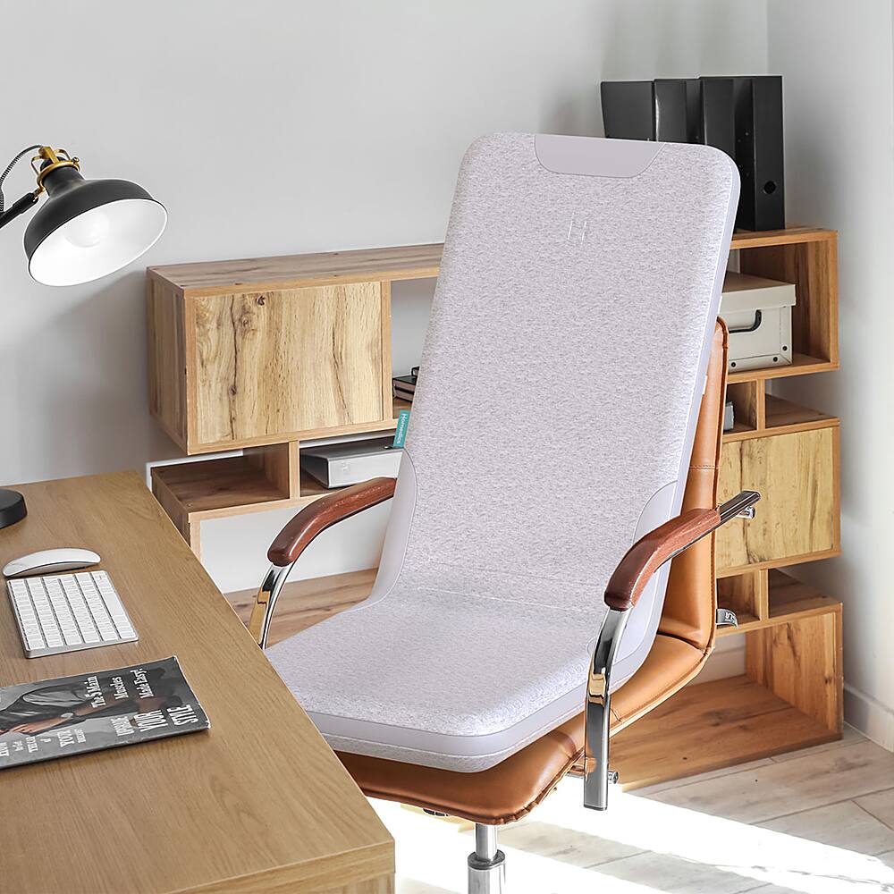 The image features a white desk chair with a wooden frame and a white cushion. The chair is positioned in front of a wooden desk, which has a keyboard and a mouse on it. There is also a book and a cup placed on the desk. The scene appears to be a workspace or a home office setup.