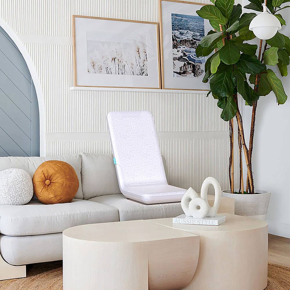 The image features a living room with a white couch and a potted plant. There is also a small white toilet with a seat cover on it, placed in the middle of the room. The room has a cozy and comfortable atmosphere, with a few decorative items such as a vase and a bowl. The presence of the toilet in the living room is an unusual and unexpected element, making it the focal point of the scene.