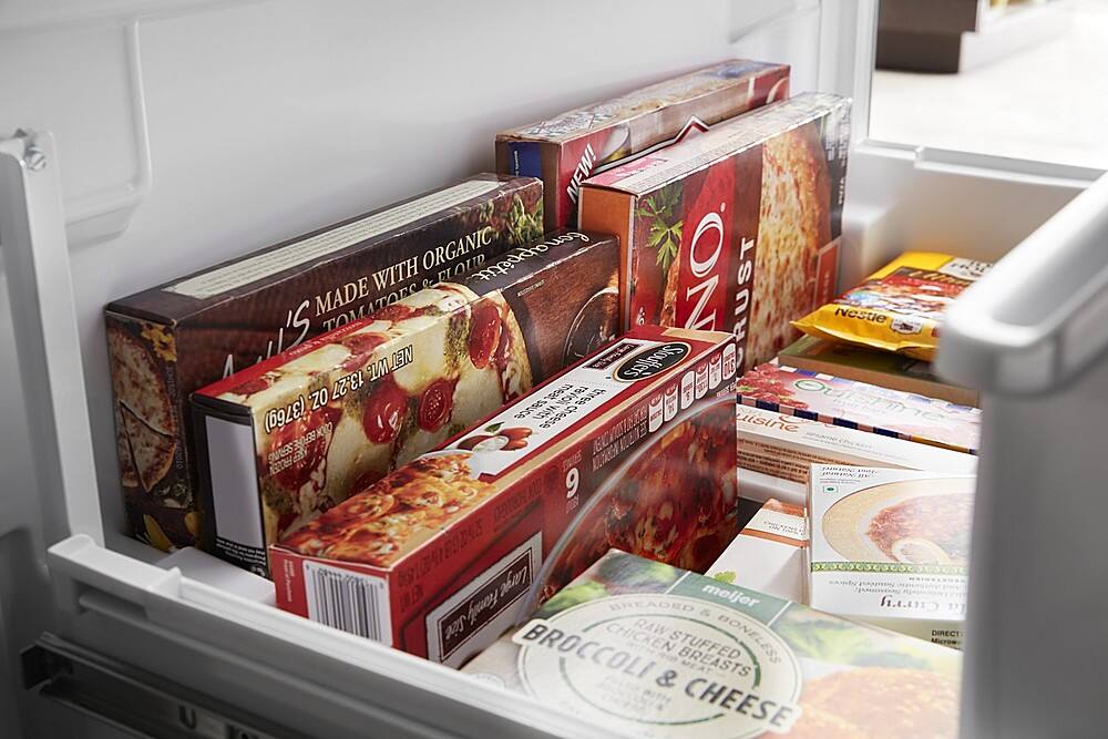 The image shows a refrigerator with its door open, revealing a variety of food items stored inside. There are several boxes of pizza, including one with the word "organic" written on it. Additionally, there are multiple bottles of sauce, and a box of broccoli can be seen among the items. The refrigerator is filled with a diverse selection of food, providing a variety of options for meal preparation.