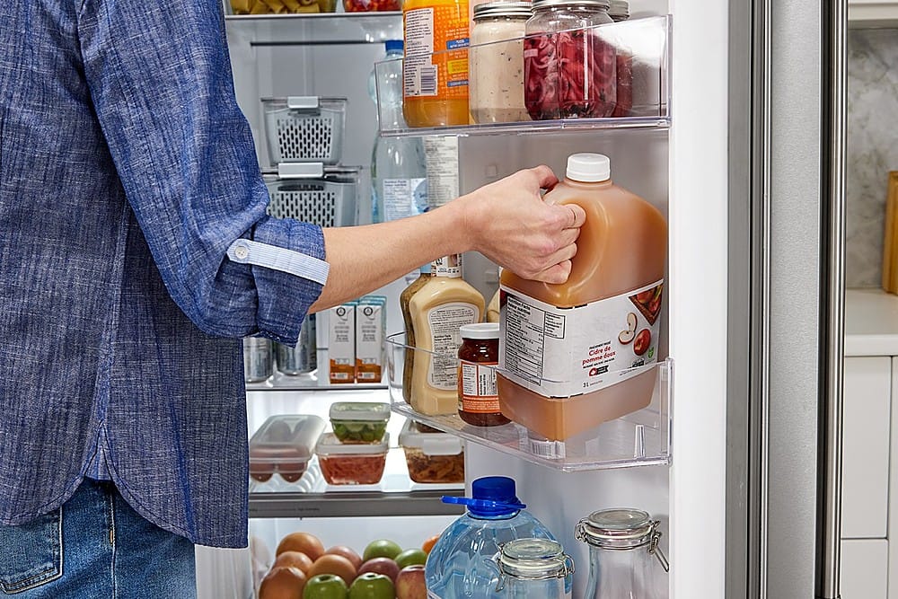 The text on the image reads "3 CILLE by - de Cidre doux pomme LE." However, this text is not in English and appears to be in a different language. The image shows a person holding a bottle of apple cider from the refrigerator.