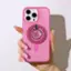The image shows a person holding a pink cell phone with a glittery case. The phone has a camera on the back, and the person is holding it up to the camera. The person's nails are painted pink, and they are wearing a pink case on their phone. The phone is a smartphone, and the person is likely taking a picture or using the camera for some purpose.