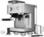 The image features a stainless steel espresso machine with a silver handle, sitting on a counter. The machine is accompanied by various kitchen items, including a measuring cup, a spoon, and a bowl. The measuring cup is placed near the espresso machine, while the spoon is located to the left of the machine. The bowl is positioned further to the right of the machine. The scene suggests a well-equipped kitchen for preparing and enjoying coffee and other beverages.