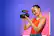 The image features a woman wearing a red tank top, holding a camera in her hands. She is smiling and appears to be enjoying herself. The camera she is holding is a Rode P-IPRENS camera, which is a high-quality video camera known for its versatility and ease of use. The woman's outfit and the camera suggest that she might be a professional photographer or videographer, or simply someone who enjoys taking pictures and recording videos.