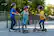 The image shows three children wearing helmets and riding scooters on a sidewalk. They are all wearing helmets for safety while enjoying their ride. The children are positioned in a row, with one child on the left, another in the middle, and the third on the right. They are all riding their scooters, likely having fun and spending time together outdoors.