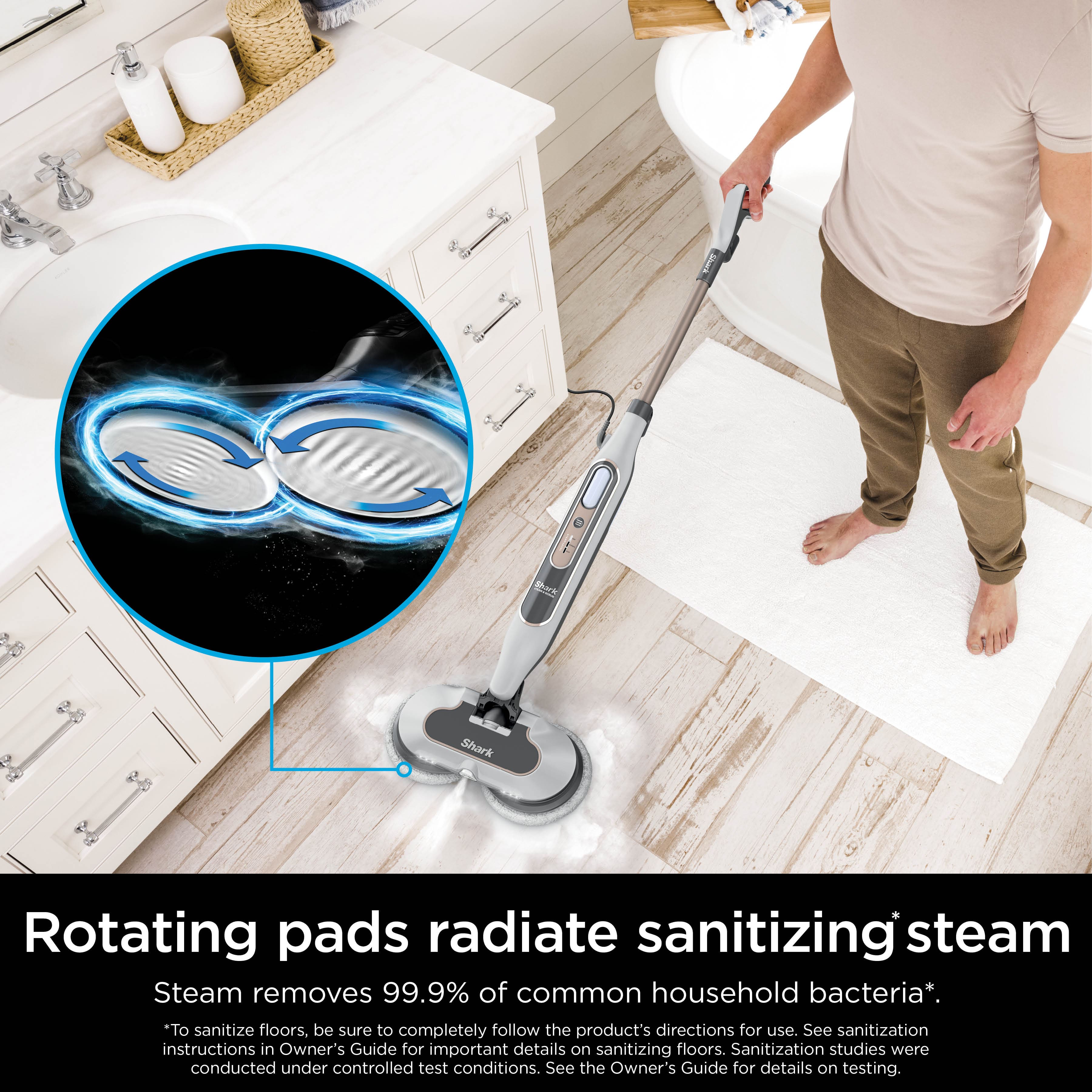 The image features a man using a steam mop to clean a bathroom floor. The mop has rotating pads that radiate sanitizing steam, which helps remove 99.9% of common household bacteria. The man is standing on a rug while using the steam mop, ensuring that the floor is thoroughly cleaned and sanitized. The image emphasizes the effectiveness of the steam mop in maintaining a hygienic and clean bathroom environment.