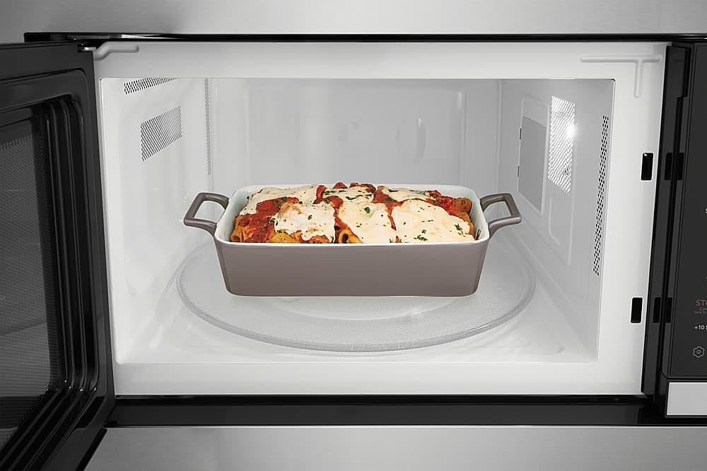 The image shows a microwave oven with a casserole dish inside. The dish contains a delicious meal, possibly lasagna, and is placed on a turntable. The microwave is open, revealing the food inside. The scene suggests that the meal is being heated or reheated in the microwave, making it ready to be enjoyed.