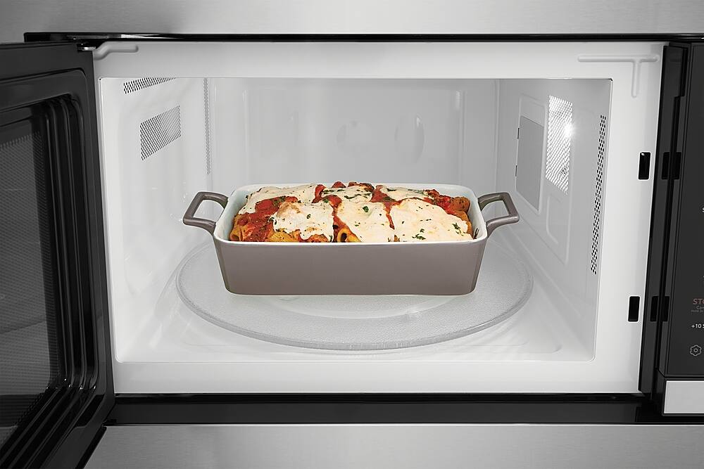 The image shows a microwave oven with a casserole dish inside. The dish contains a delicious meal, possibly lasagna, and is placed on a turntable. The microwave is open, revealing the food inside. The scene suggests that the meal is being heated or reheated in the microwave, making it ready to be enjoyed.