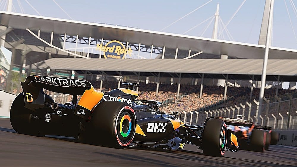 The image features a racing car with the word "Darktrace" on the back, indicating that it is sponsored by the company. The car is driving on a track, and there are several people watching the race. The scene is set in a stadium, with the car racing down the track and the audience eagerly watching the action.