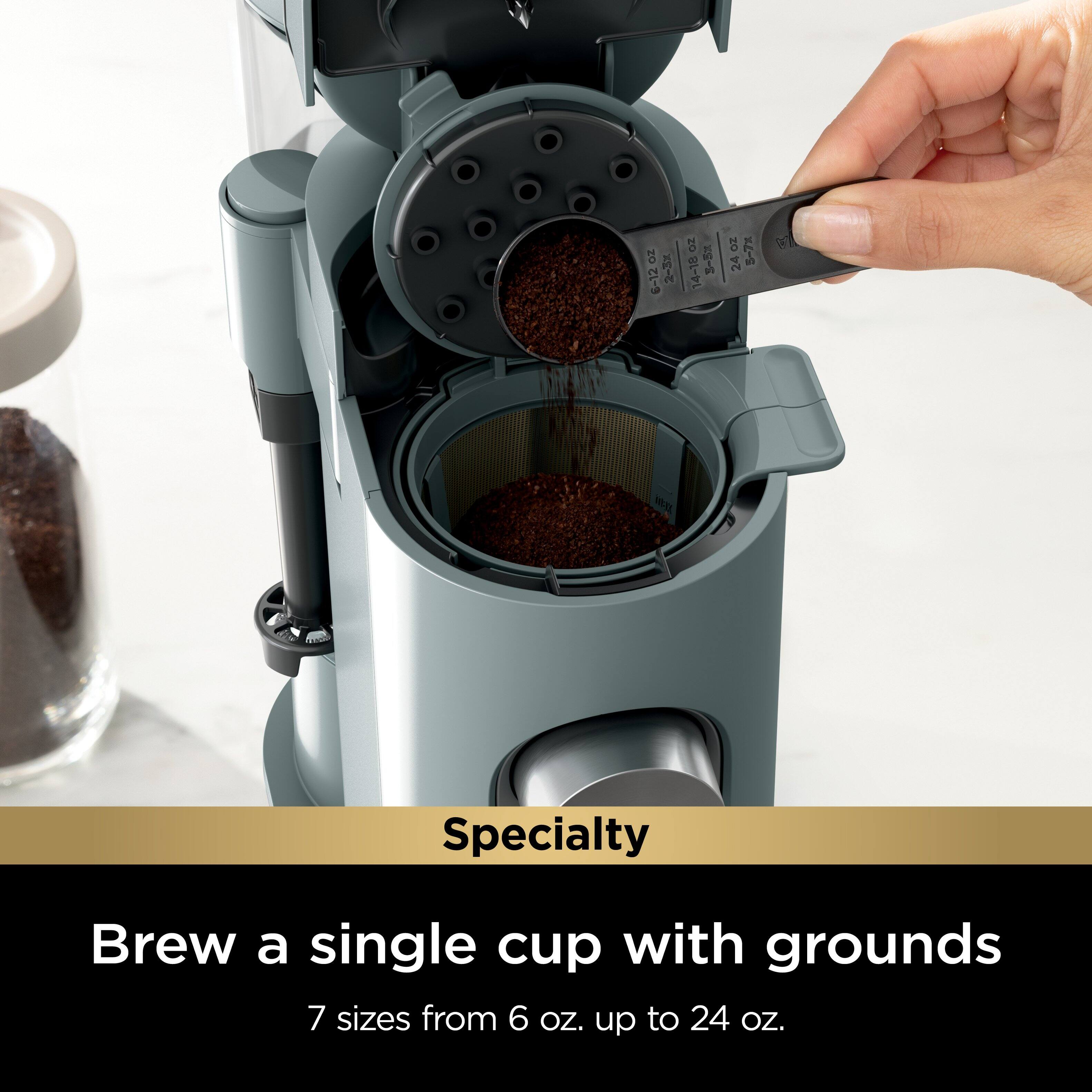 The image features a person using a coffee maker to brew a single cup of coffee with grounds. The coffee maker is a specialty machine designed for this purpose, offering 7 different sizes from 6 oz. up to 24 oz.