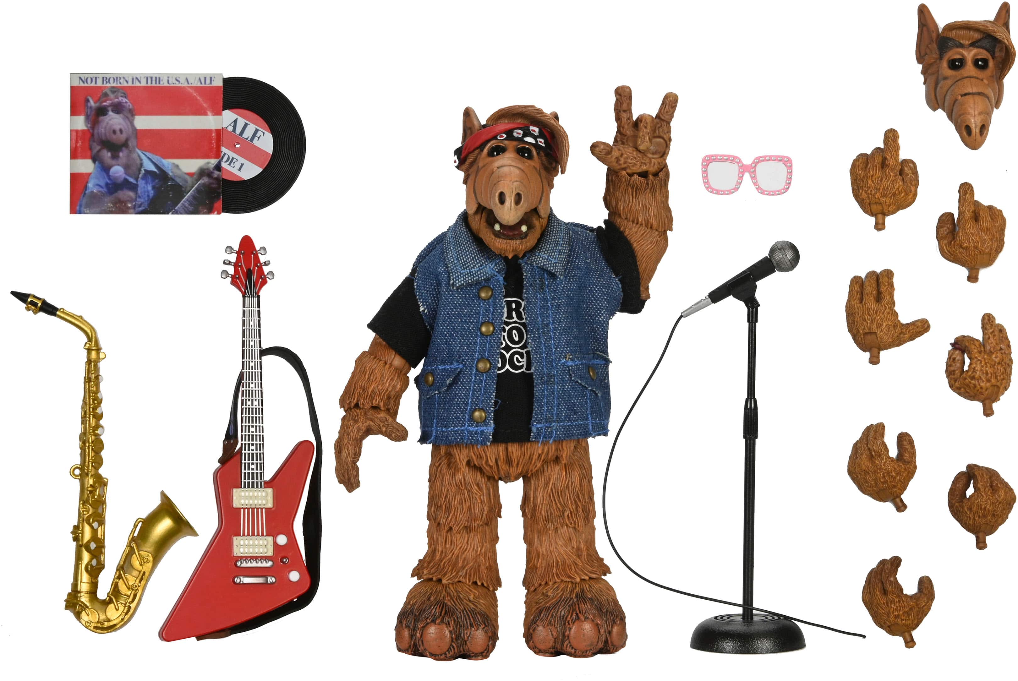 The image features a stuffed animal, likely an Alf doll, posed with a guitar and a microphone. The doll is wearing a denim vest and a red bandana. The scene also includes a saxophone, a pair of glasses, and a few other accessories. The doll is giving a peace sign, creating a fun and playful atmosphere.