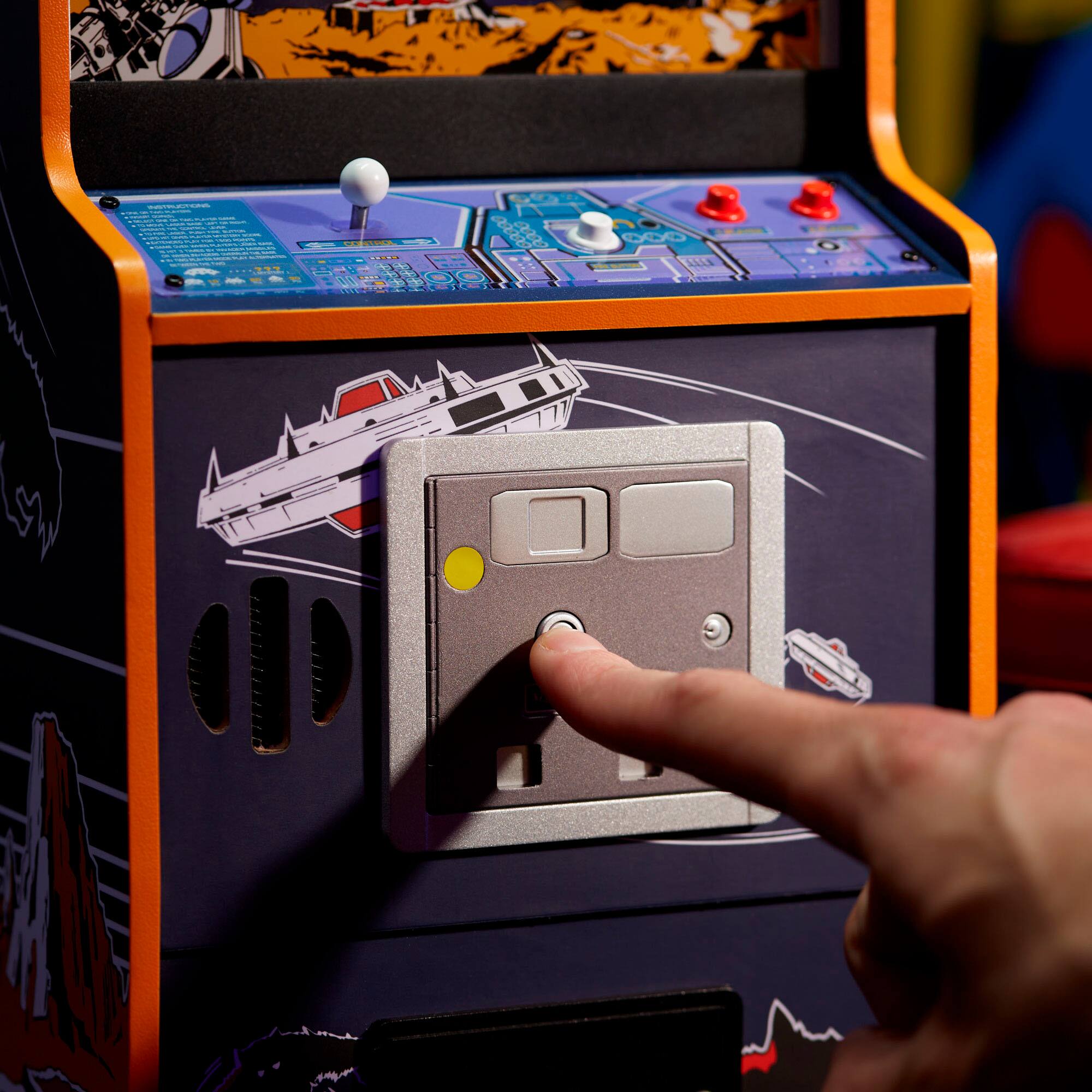 The image shows a person pressing a button on a machine, which is likely a video game or arcade game. The button is located on the side of the machine, and the person's hand is clearly visible as they push it. The machine is decorated with a space theme, featuring a rocket ship on the front. The person's hand is positioned near the button, indicating that they are actively engaging with the machine.