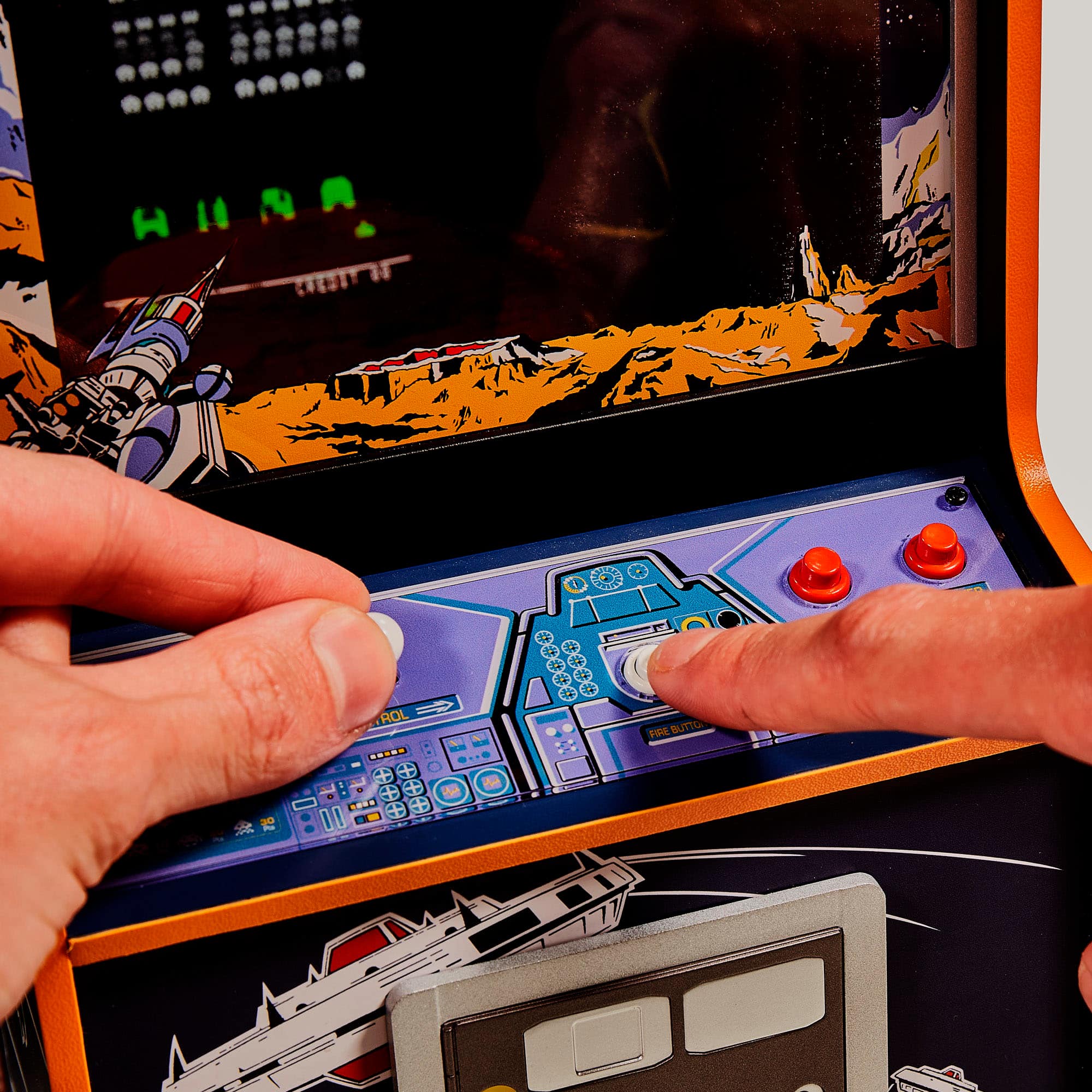 The image shows a person playing a video game on a machine, likely an arcade game, with a spaceship on the screen. The person is using a joystick to control the game, and their hand is on the joystick. The game appears to be a space shooter, as the person is using a spaceship to navigate through the game. The machine has a colorful background, adding to the overall visual appeal of the game.