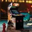 The image features a Teenage Mutant Ninja Turtles arcade machine, which is a large video game machine with a screen and buttons. The machine is placed in a dark room, and there is a fire hydrant nearby. The machine is designed to look like a TMNT game, and it is likely a popular attraction for fans of the franchise.