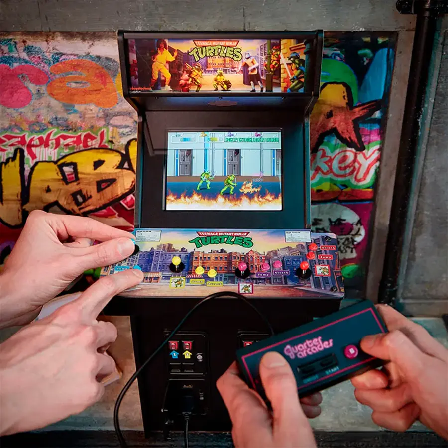 The image shows two people playing a video game on a Teenage Mutant Ninja Turtles arcade machine. The machine is placed on a wall, and the players are using remote controls to play the game. The game appears to be a popular choice among arcade enthusiasts, as it is a classic and well-known game. The players are likely enjoying the nostalgic experience and the challenge of mastering the game's mechanics.