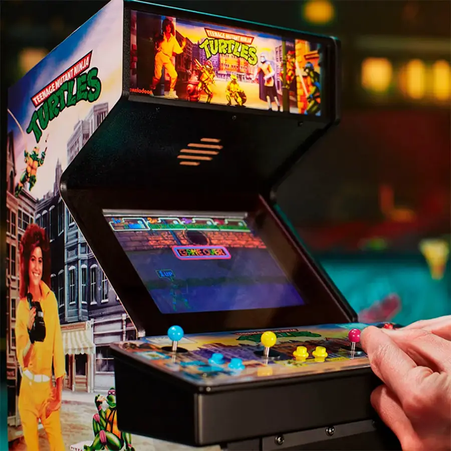The image features a person playing a video game on a Teenage Mutant Ninja Turtles arcade machine. The machine has a large screen and buttons for controlling the game. The person is holding a joystick, which is used to play the game. The game is likely a popular arcade game from the 1990s, as it is based on the Teenage Mutant Ninja Turtles franchise.