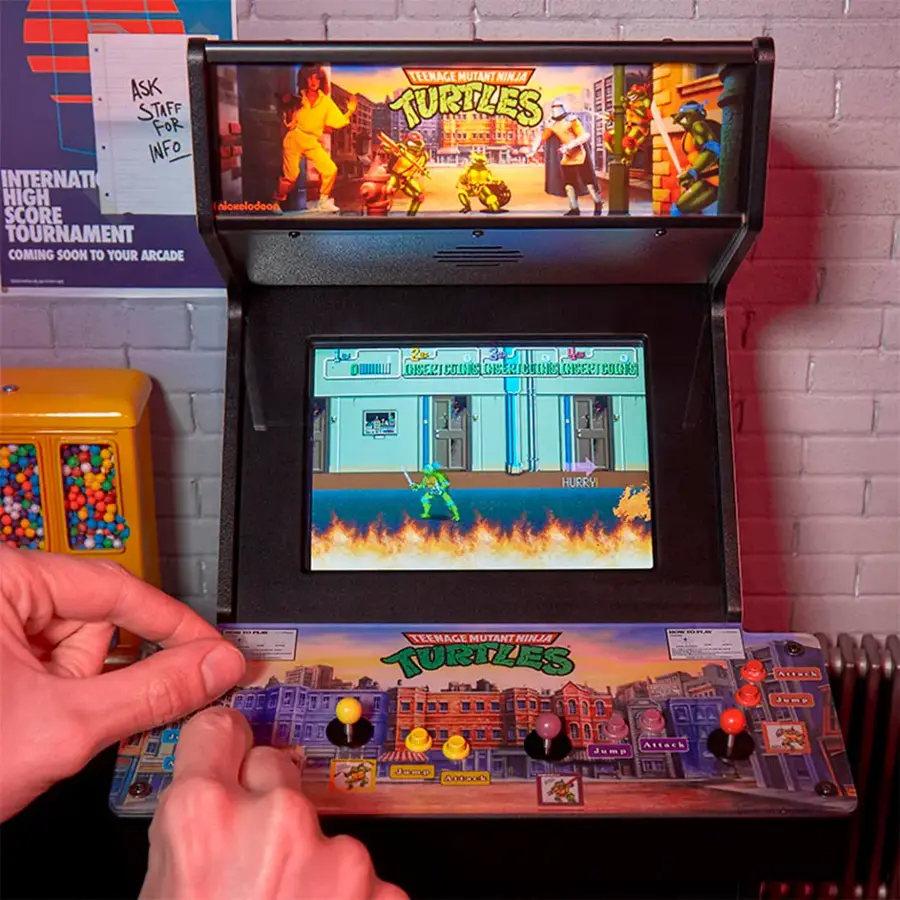 The image features a person playing a video game, specifically Teenage Mutant Ninja Turtles, on a Nintendo machine. The game is displayed on a large screen, and the person is using a joystick to control the game. The scene takes place in an arcade setting, where the game is likely part of a tournament or event. The game is set to start soon, and players are encouraged to join in the fun.