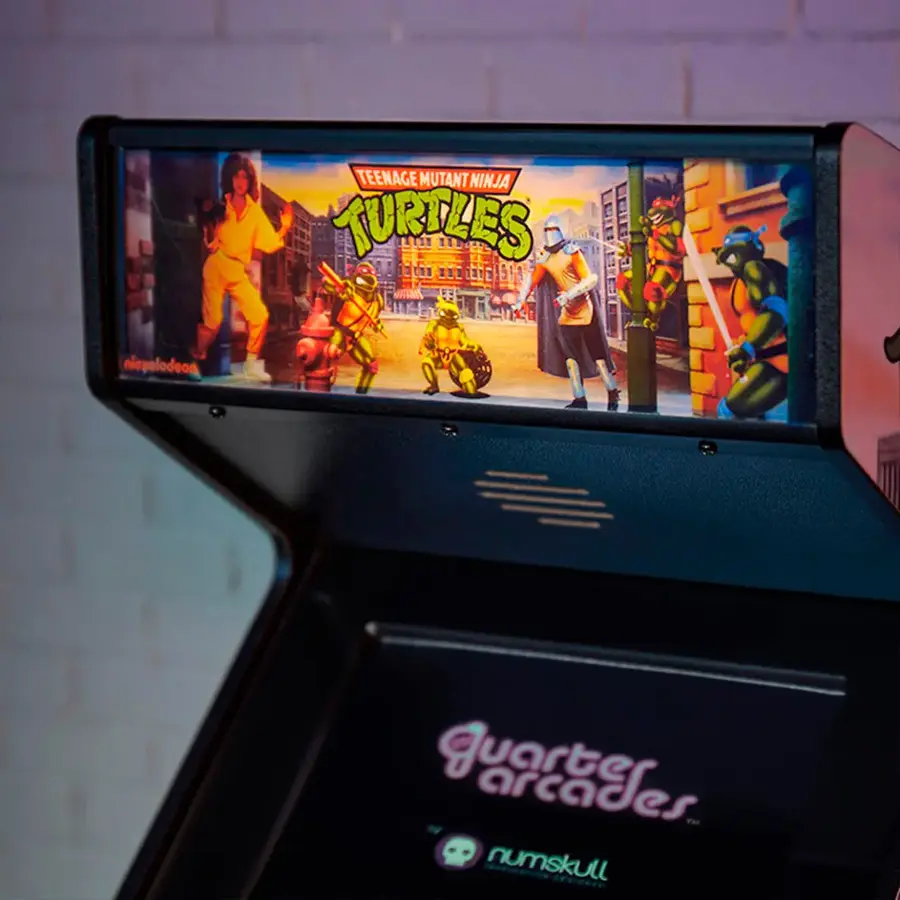 The image features a Teenage Mutant Ninja Turtles arcade machine. The machine is black and has a screen displaying the game. The game is likely a quarter arcade game, as it is designed for short play sessions and requires players to insert coins to play. The machine is placed in a brick building, possibly a mall or an arcade.