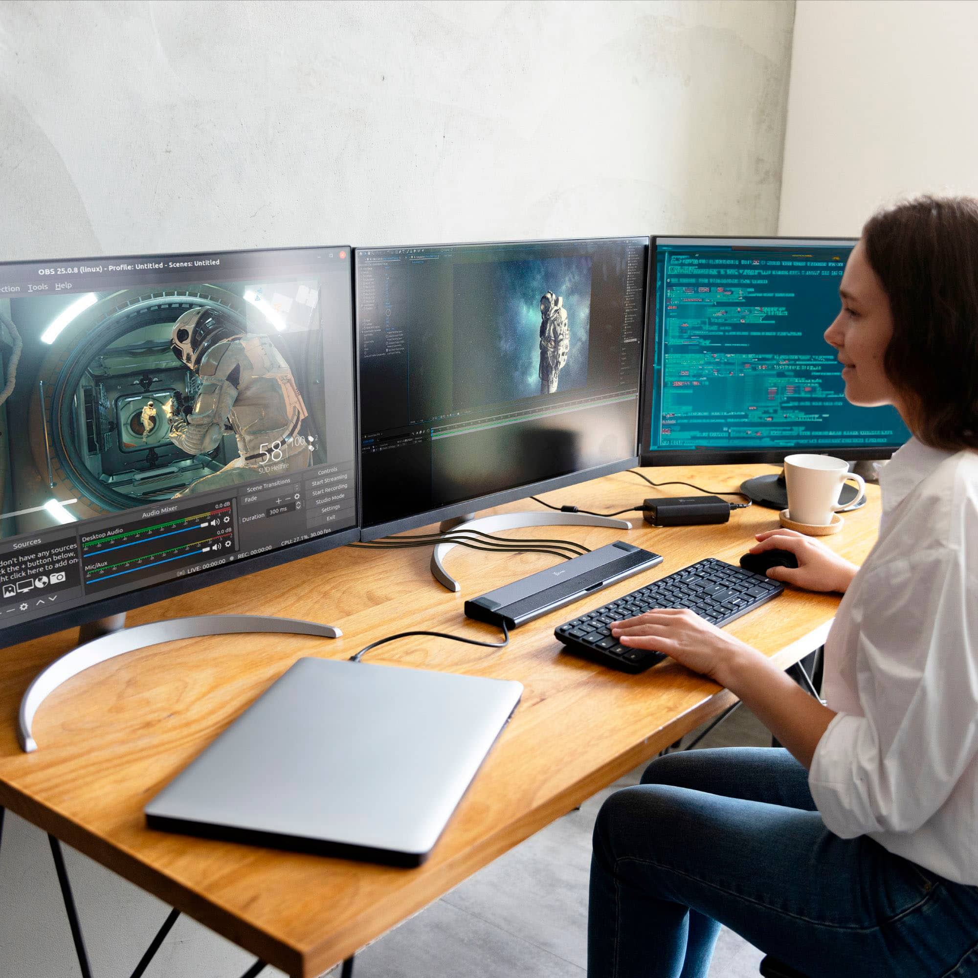 The image shows a woman sitting at a desk with a laptop and a keyboard. She is using the laptop, which is connected to a docking station. The desk also has a mouse and a cup. The woman appears to be focused on her work or task at hand.