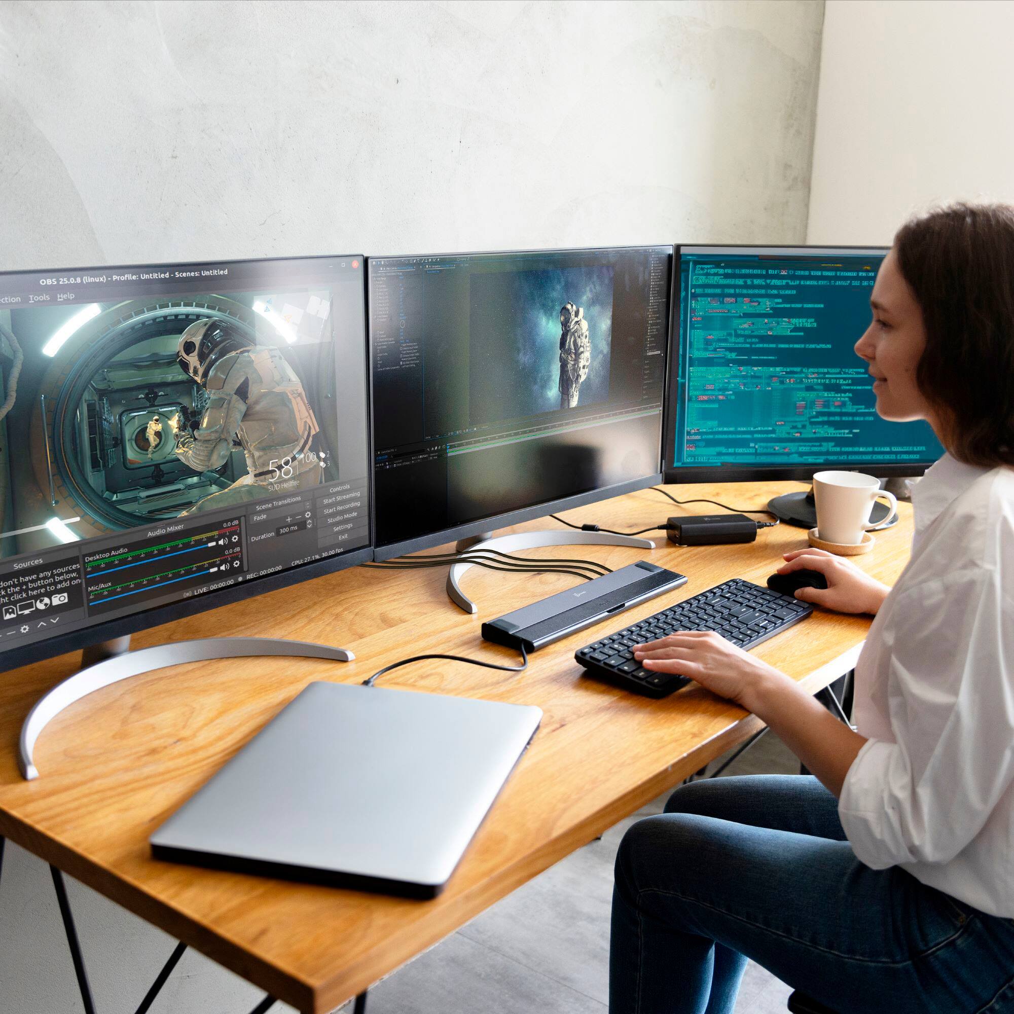 The image shows a woman sitting at a desk with a laptop and a keyboard. She is using the laptop, which is connected to a docking station. The desk also has a mouse and a cup. The woman appears to be focused on her work or task at hand.