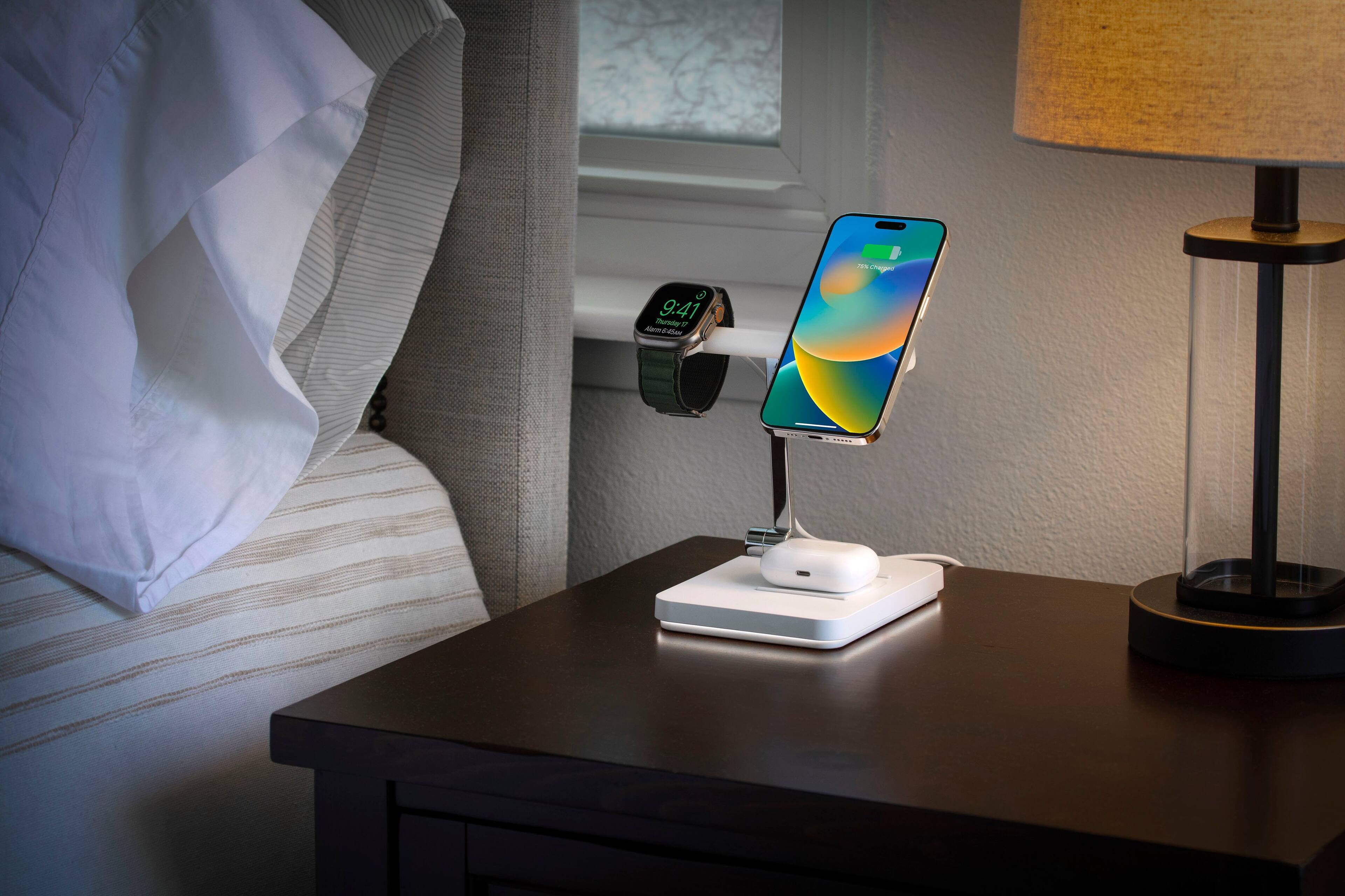 The image features a bed with a white pillow and a cell phone placed on a stand. The cell phone is positioned in front of a window, and it is currently displaying the time of 9:41. The stand is designed to hold the phone at an angle, making it easy to view and interact with the device.