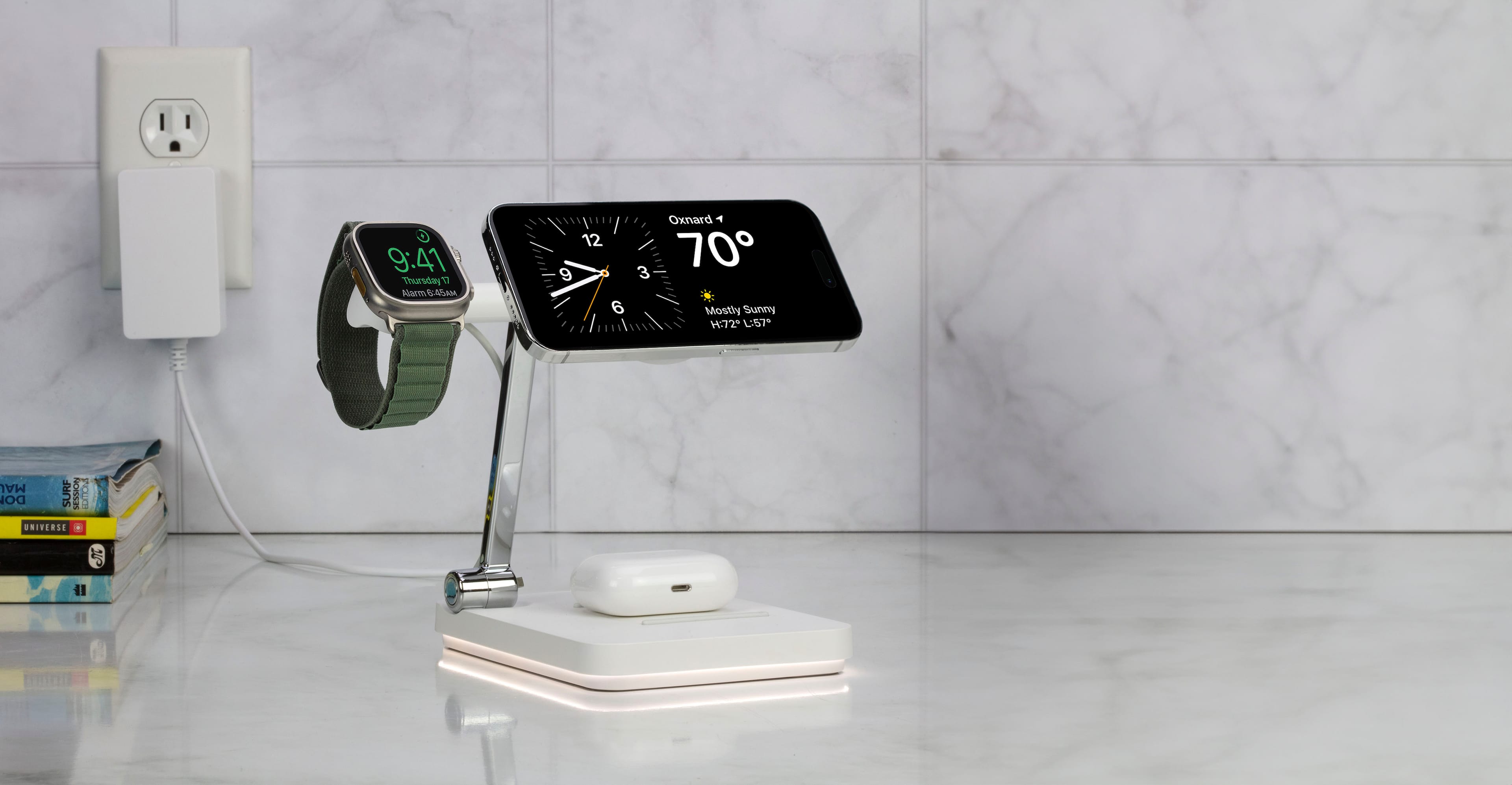 The image shows a clock displaying the time as 9:41 on a Thursday. The clock is mounted on a wall, and there is a cell phone nearby. The cell phone is charging, and there is a book placed on the table. The scene suggests a typical home or office setting where someone is likely working or studying.