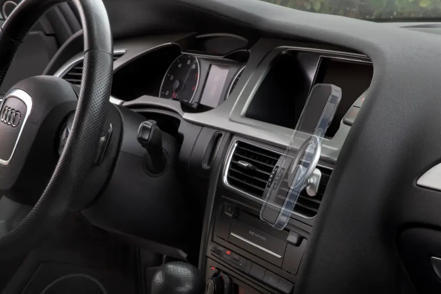The image shows the interior of a car with a steering wheel and a dashboard. The dashboard has a clock and a speedometer, and there is a small car air freshener hanging from the dashboard. The car is equipped with a radio, and the steering wheel is positioned close to the dashboard. The car appears to be a luxury model, possibly an Audi, with a focus on the multimedia system.