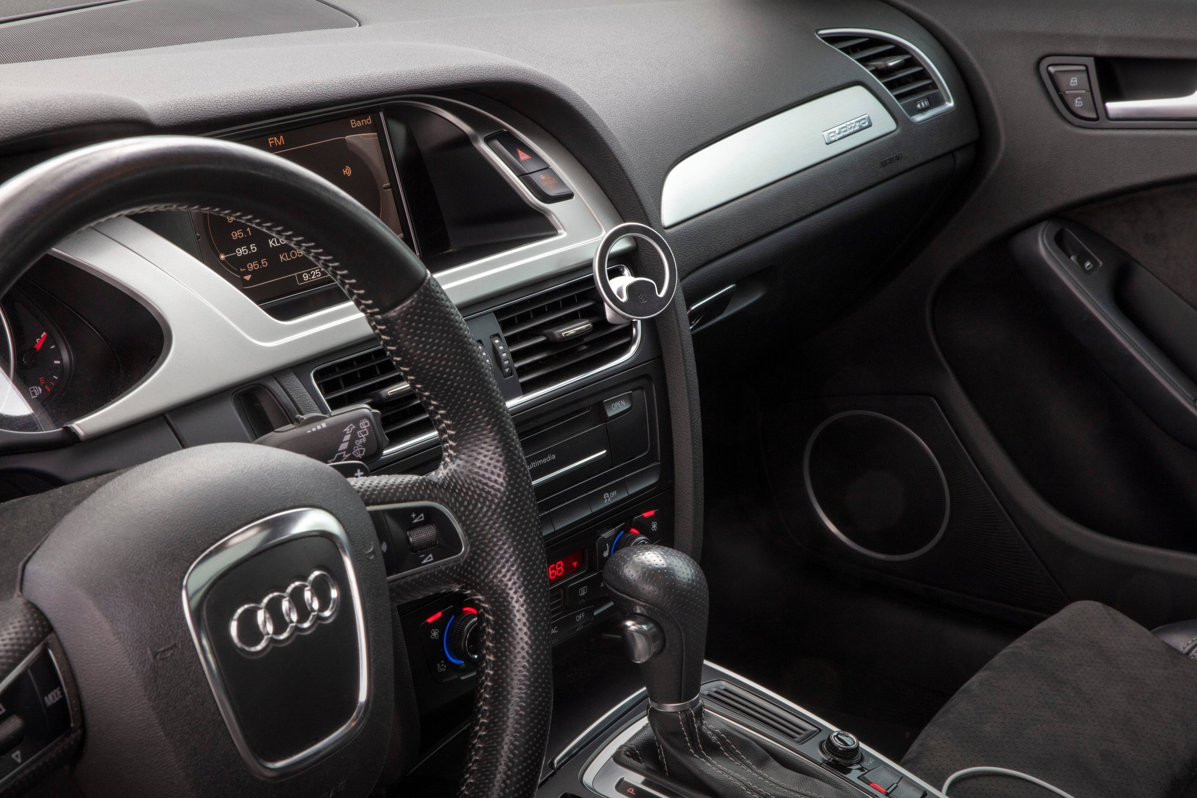 The image shows the interior of a car with a steering wheel and a dashboard. The dashboard displays the radio station, which is currently tuned to KLOS. The car is parked, and the driver's seat is empty. The car is equipped with an Audi sound system, and the radio is set to FM band.