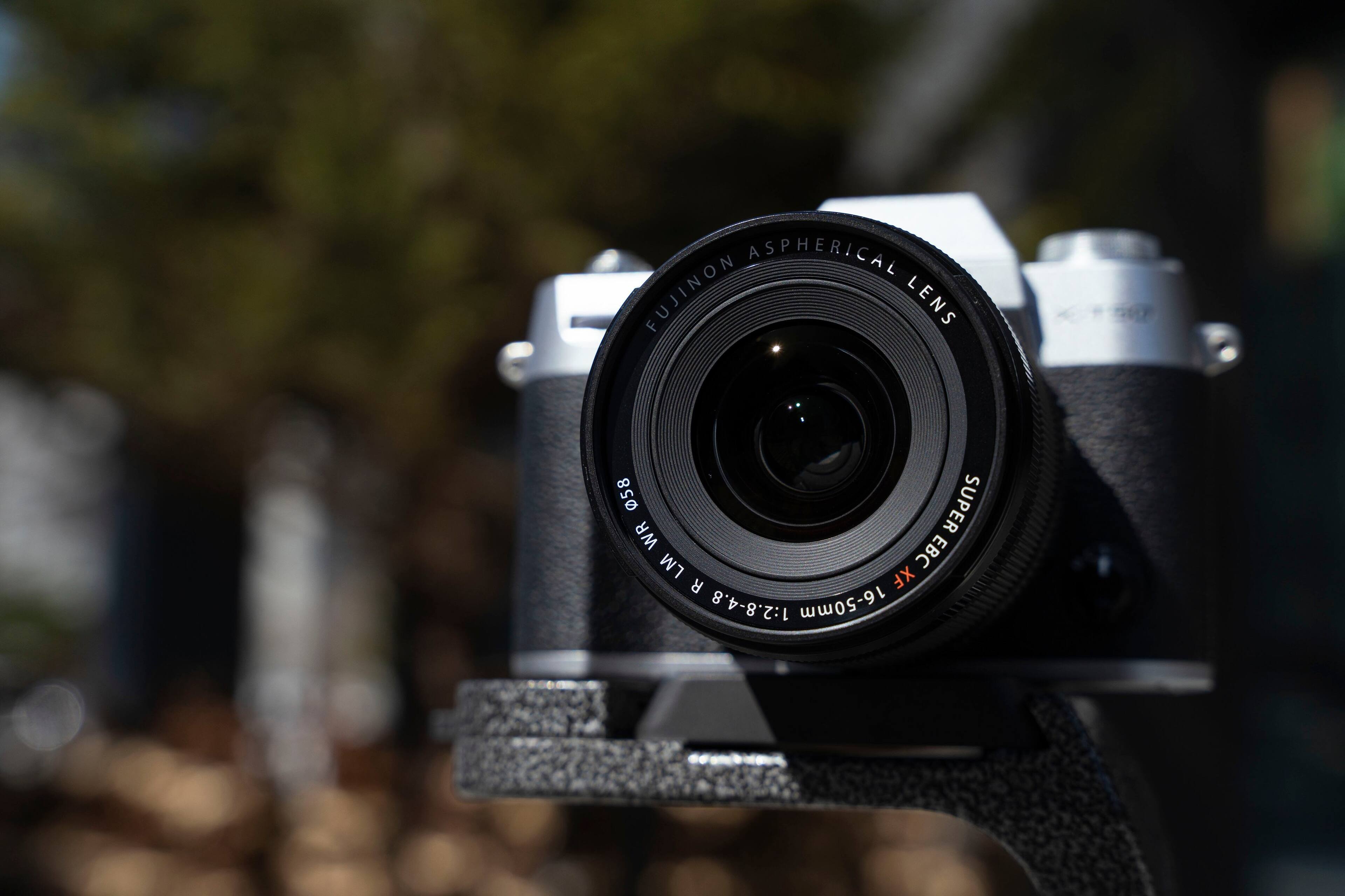 The image features a close-up of a digital camera with a large lens. The lens is an aspherical Fujinon lens with a focal length of 16-50mm and aperture of 1:2.8-4.8. The camera is mounted on a tripod, providing stability for capturing images. The image is categorized as Digital_Cameras.