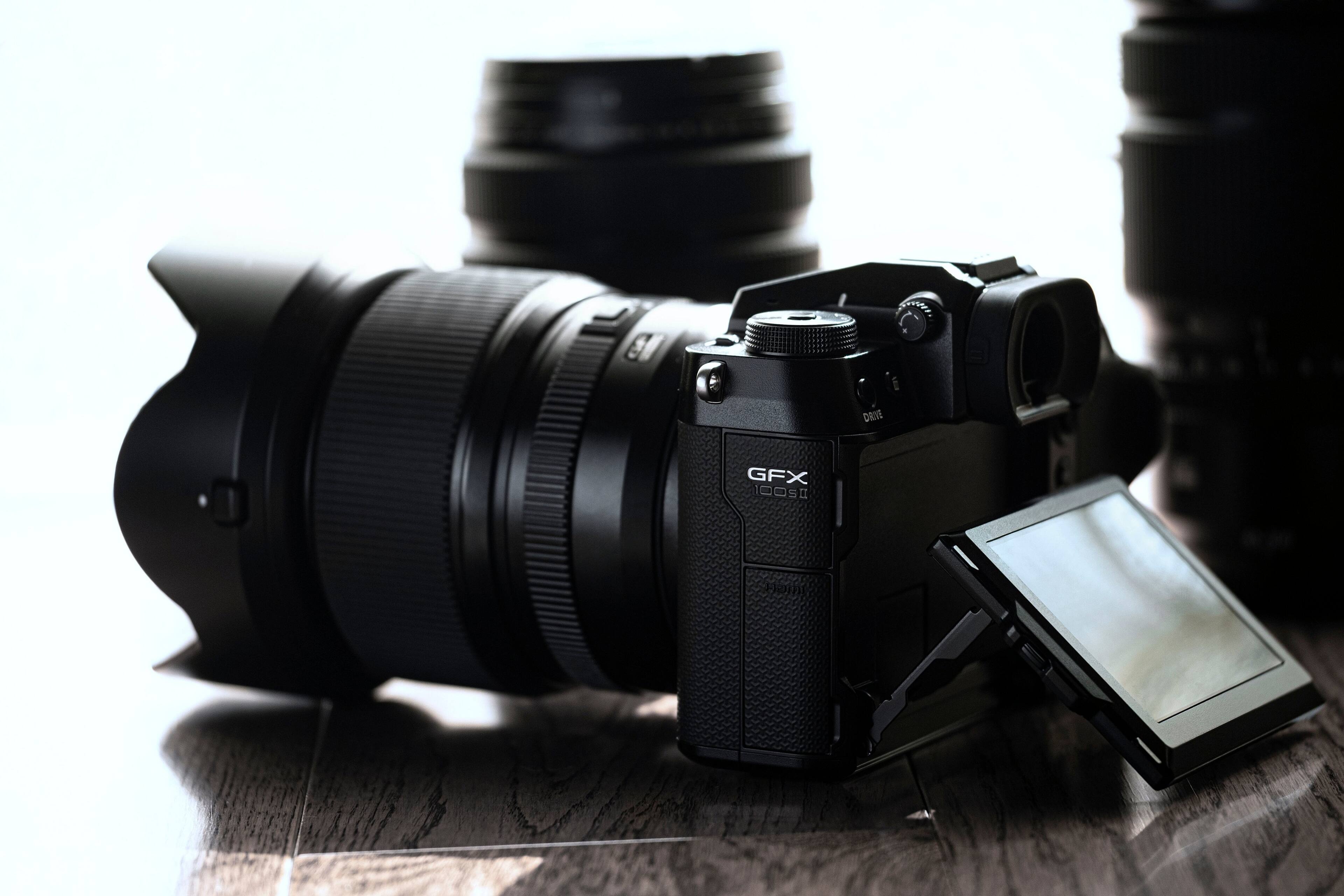 The image features a large camera lens sitting on a wooden table. The lens is accompanied by a smaller camera, possibly a smartphone, which is placed on top of the lens. The scene suggests that the photographer is using both the large camera and the smartphone for different purposes, such as capturing high-quality images with the large lens and using the smartphone for additional features or convenience.