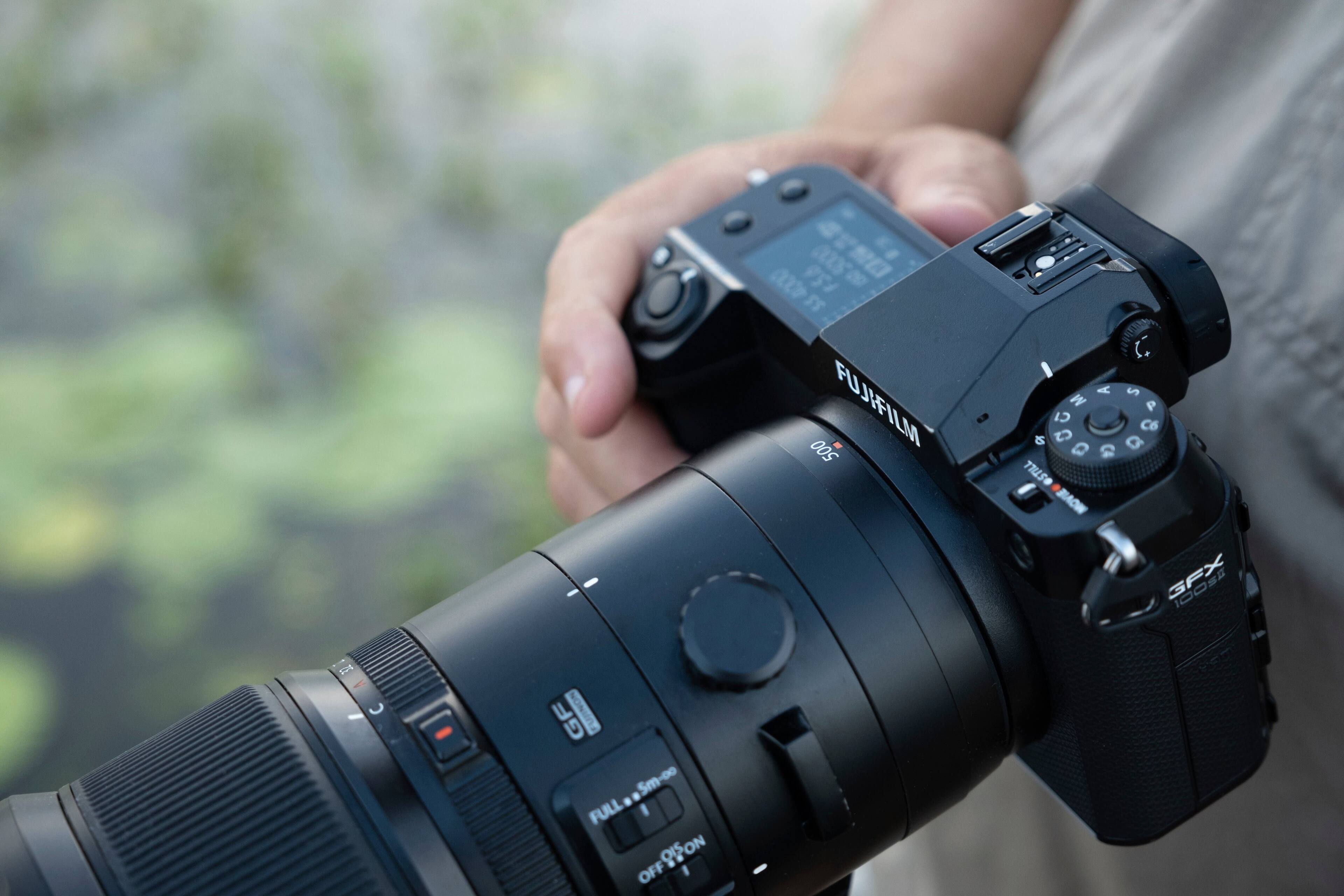 The image features a person holding a camera, which is described as a "digital camera." The camera is being held up to the sky, possibly for a better view or to capture a specific scene. The person is also holding a remote control, which suggests that they might be using it to operate the camera or control other devices. The scene appears to be set outdoors, with the camera and remote control being the main focus of the image.