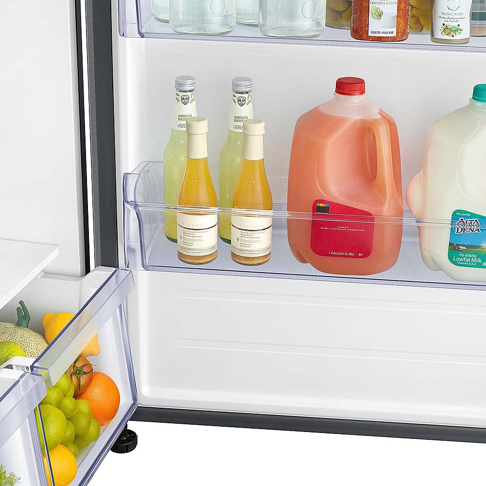 The image shows a refrigerator with a variety of drinks and food items. There are several bottles of wine and juice, as well as a bottle of milk. The refrigerator also contains a few oranges and apples. The refrigerator is open, revealing the contents inside.