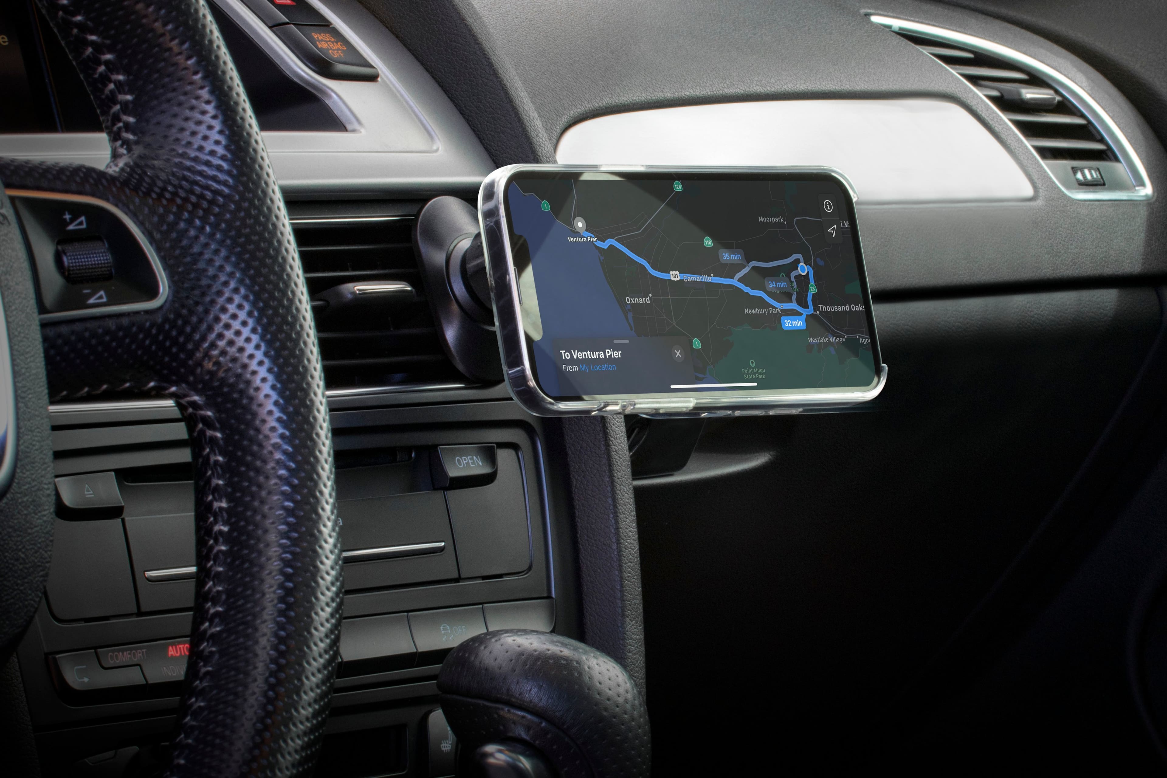 The image shows a car's dashboard with a cell phone mounted on it. The phone is displaying a map, showing the route from Moorpark to Oxnard. The map also shows the distance and estimated time of arrival at the destination. The car's steering wheel is visible in the foreground, and the dashboard is equipped with a GPS system.