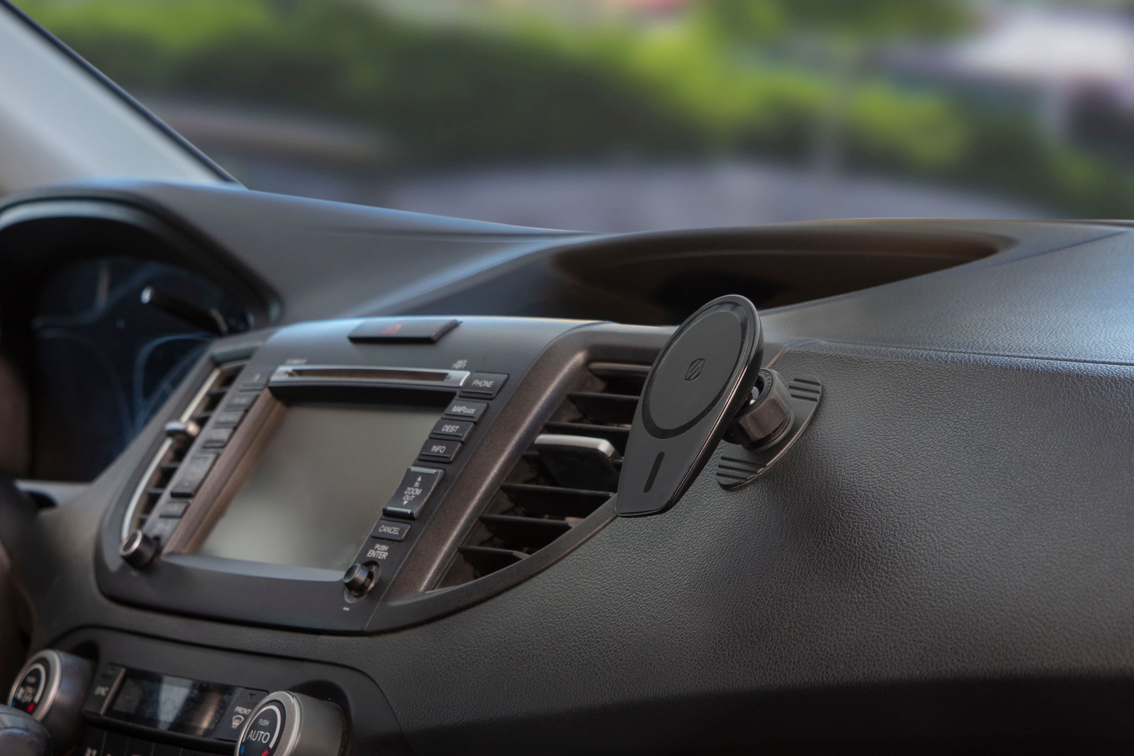 The image shows the inside of a car with a dashboard and a steering wheel. The dashboard features a radio with a small screen, and there is a small round object attached to the dashboard. The steering wheel is positioned close to the dashboard, and the car's interior appears to be made of leather.