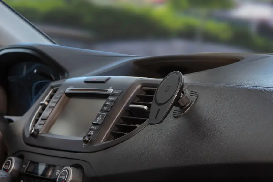 The image shows the inside of a car with a dashboard and a steering wheel. The dashboard features a radio with a small screen, and there is a small round object attached to the dashboard. The steering wheel is positioned close to the dashboard, and the car's interior appears to be made of leather.