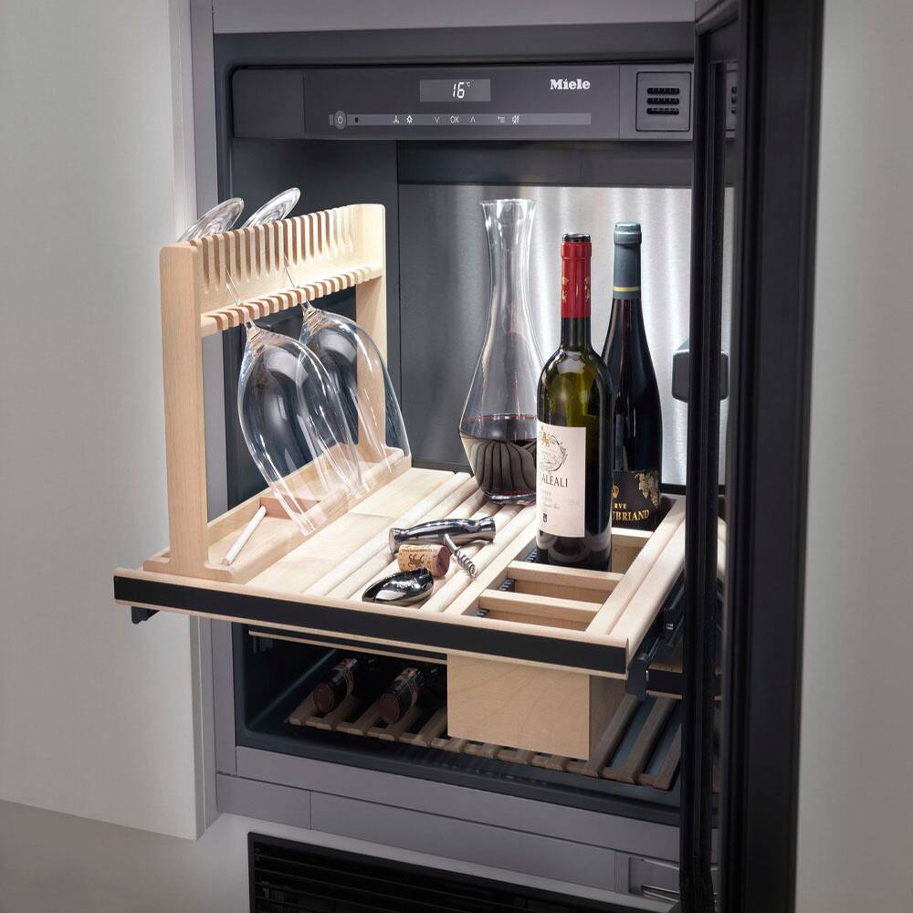 The image features a wine refrigerator with a variety of wine bottles and glasses stored inside. There are at least five wine bottles of different sizes and shapes, with one prominently placed in the center of the refrigerator. Additionally, there are three wine glasses, with one on the left side, one on the right side, and another one in the middle. The refrigerator is filled with these wine bottles and glasses, showcasing a diverse collection of wine items.