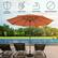 The image features a large orange umbrella, which is placed on a wooden deck near a swimming pool. There are two chairs in the scene, one on the left side and another on the right side of the umbrella. The umbrella is described as durable, easy to use, stable, and having a base not included.