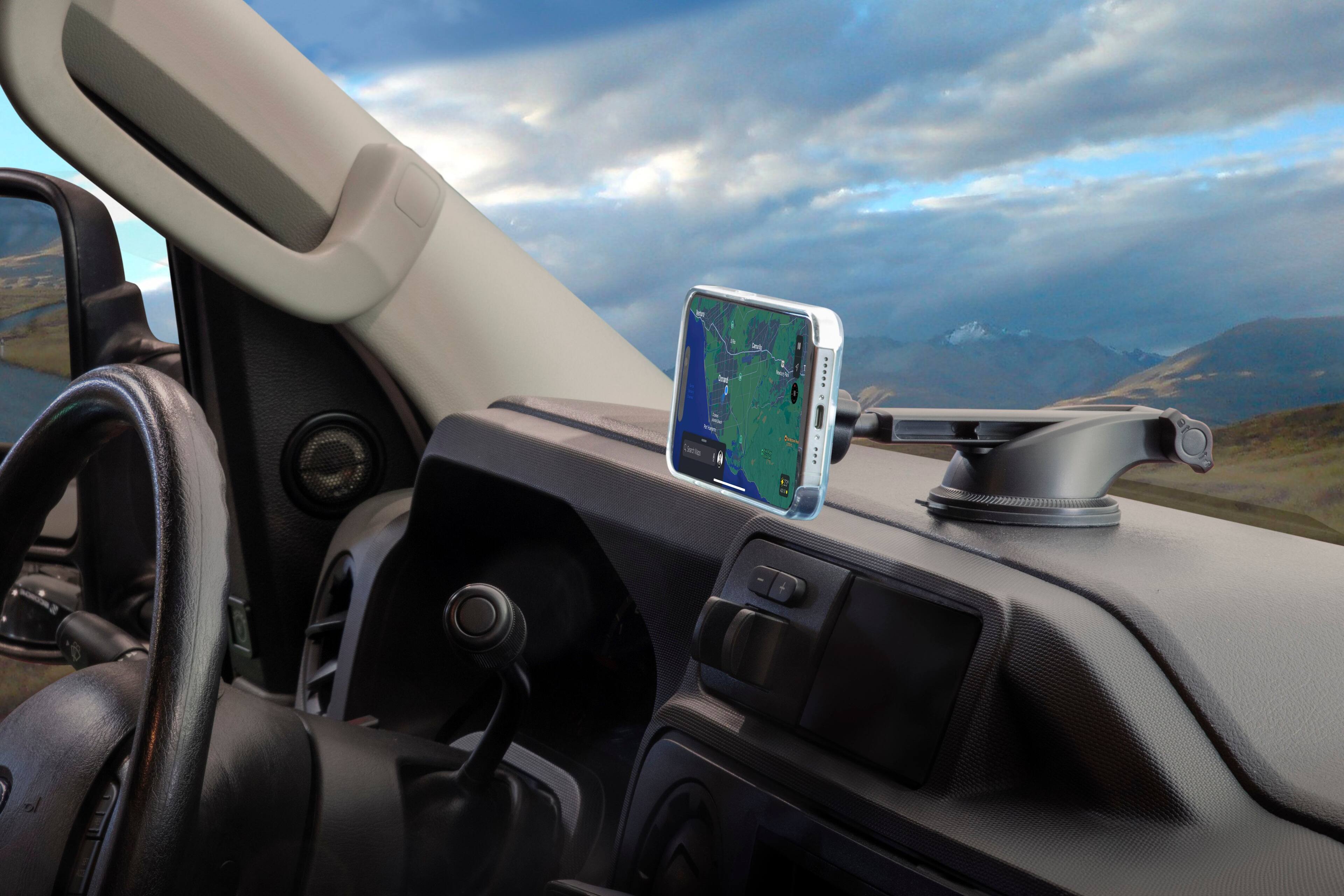 The image shows a car with a cell phone mounted on the dashboard, displaying a map. The car is parked near a body of water, possibly a lake, and there is a mountain in the background. The scene appears to be a picturesque outdoor setting, with the car's interior providing navigation assistance for the driver.